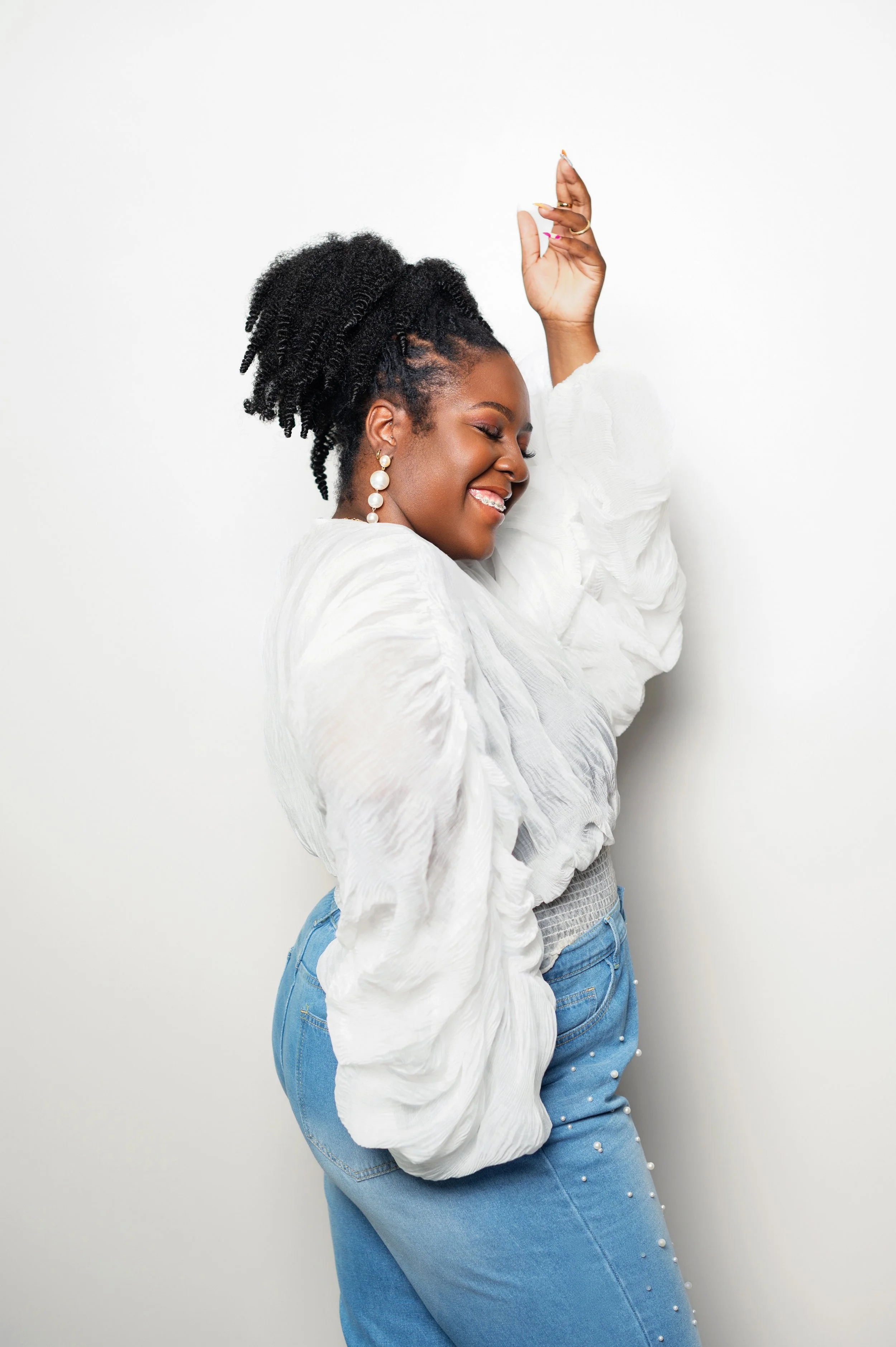Raven Ponder stands in a white room wearing a whte blouse, smiling with a calm, confident expression
