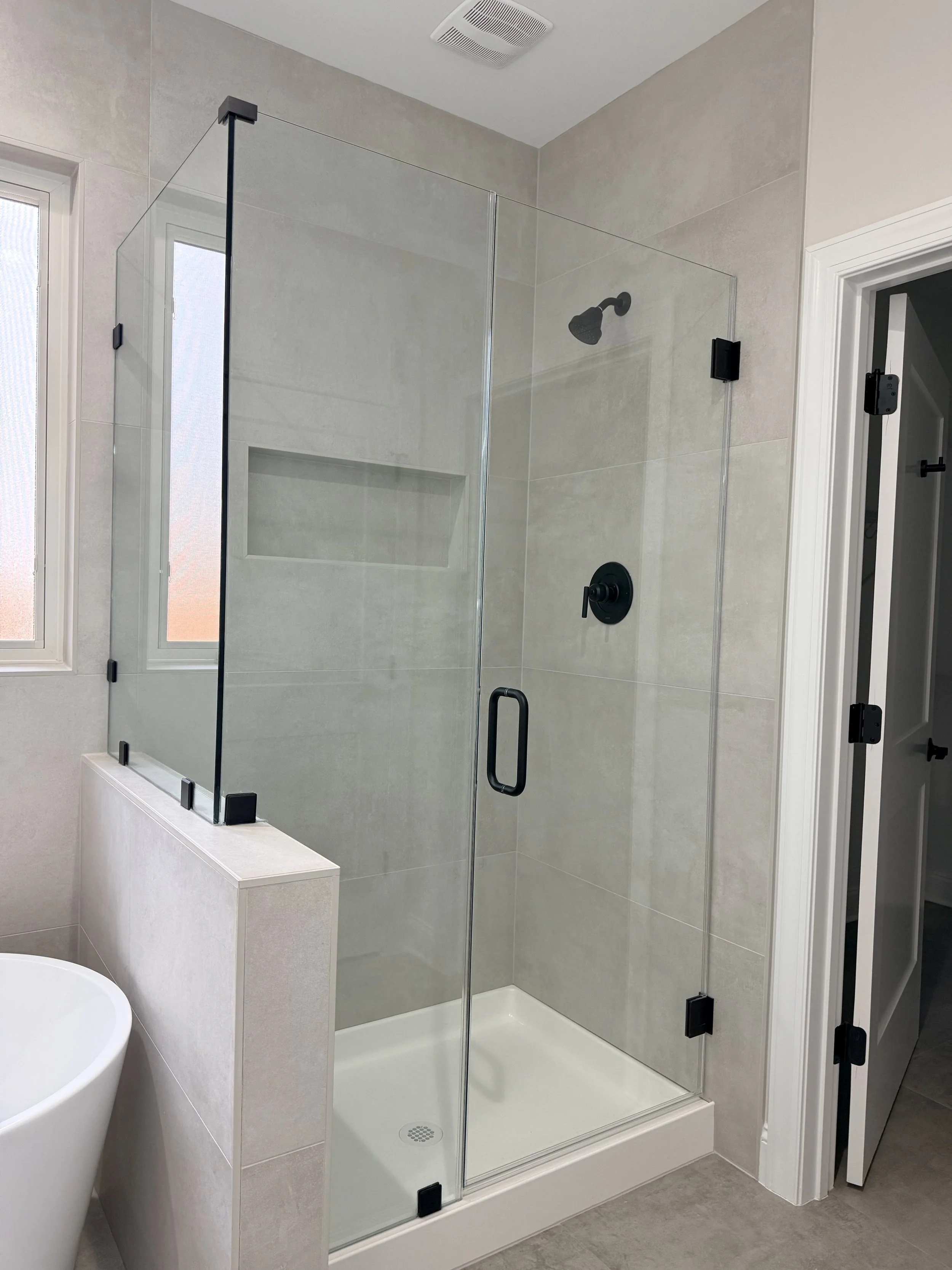 Modern bathroom with a glass shower enclosure, black fixtures, a niche in the shower wall, a window, and part of a white toilet.