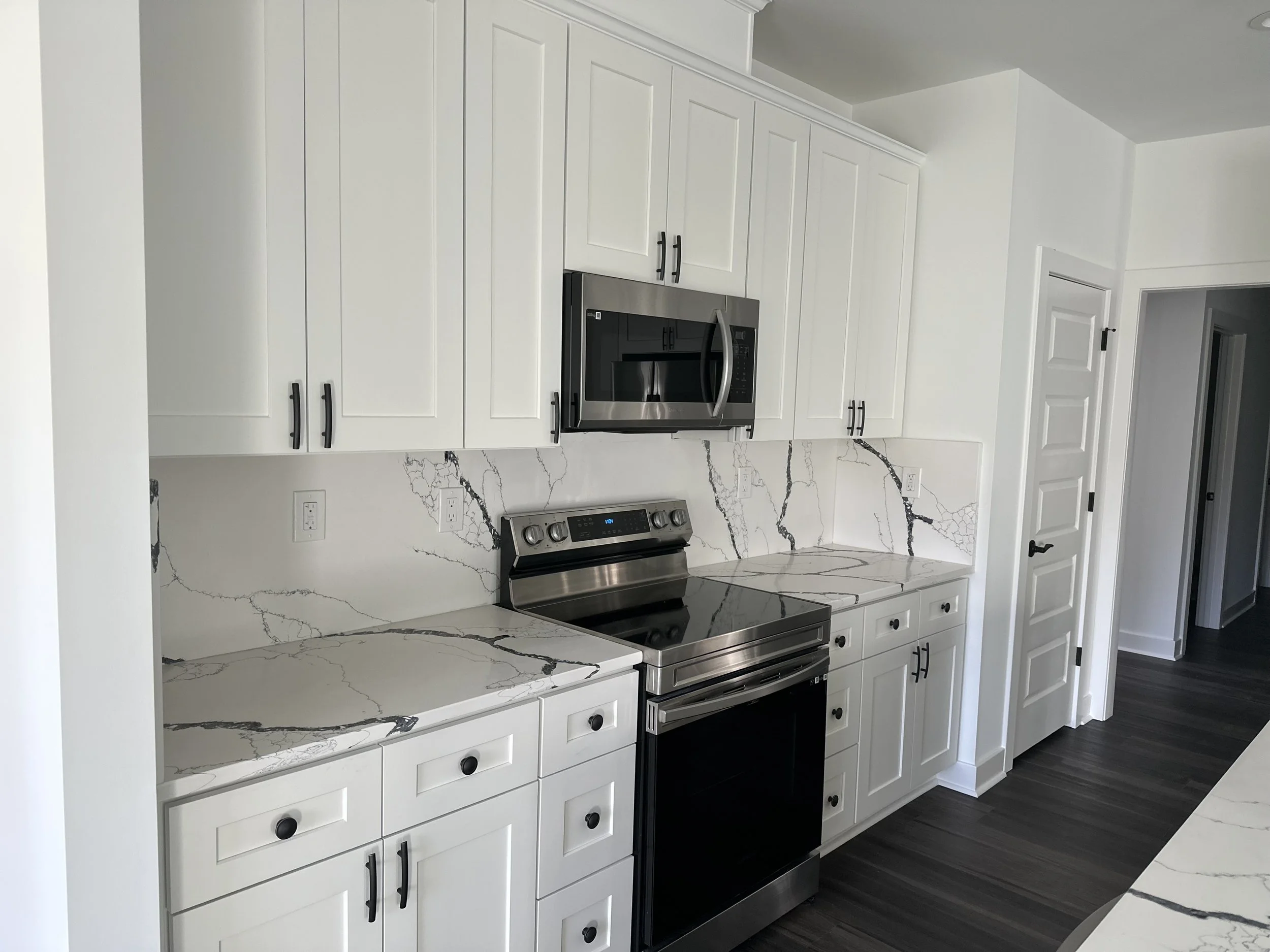 Modern kitchen with white cabinets, black hardware, marble countertops, and a stainless steel stove and microwave.