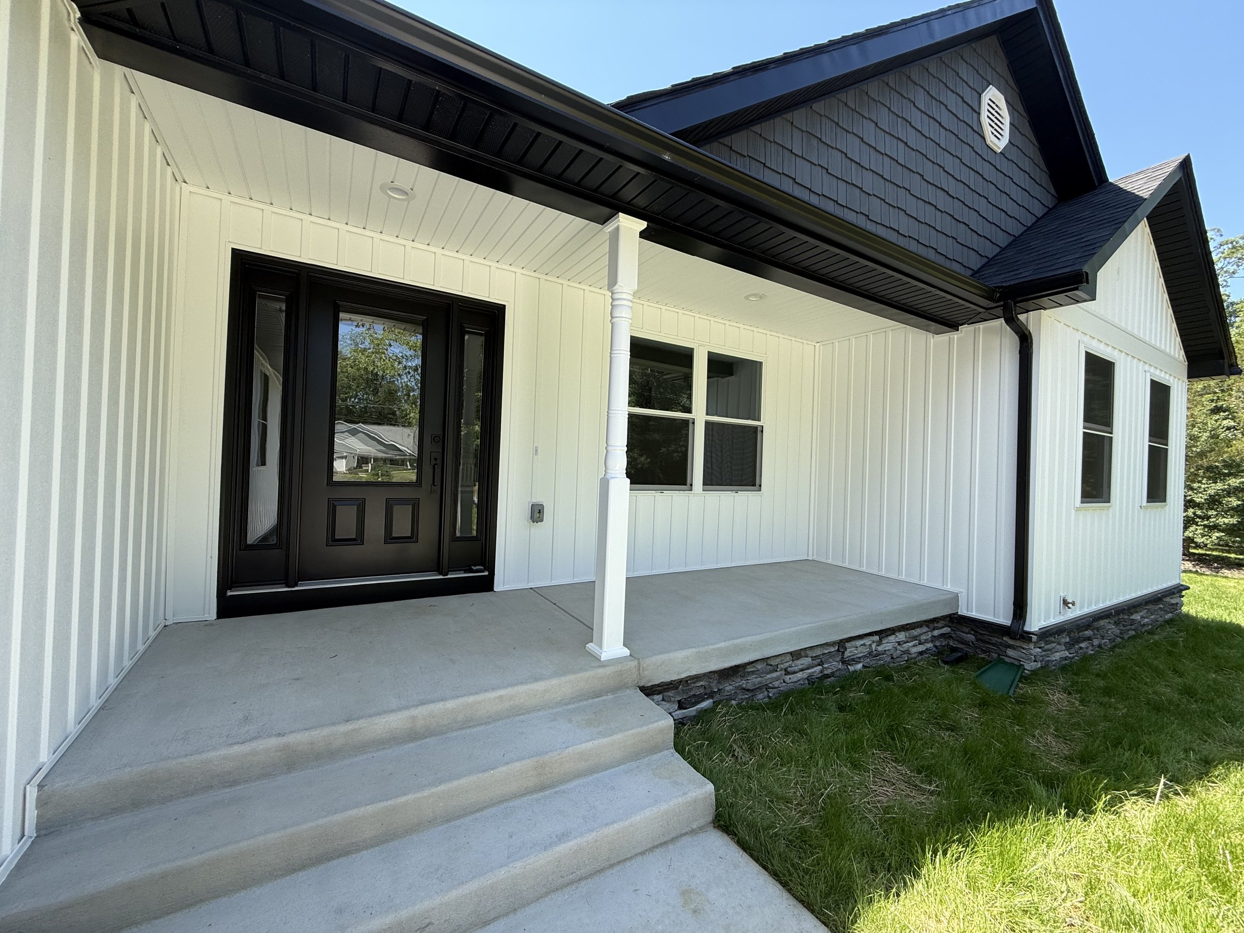 Front porch of a new house with black door, white siding, gray stone foundation, and steps leading to the porch.