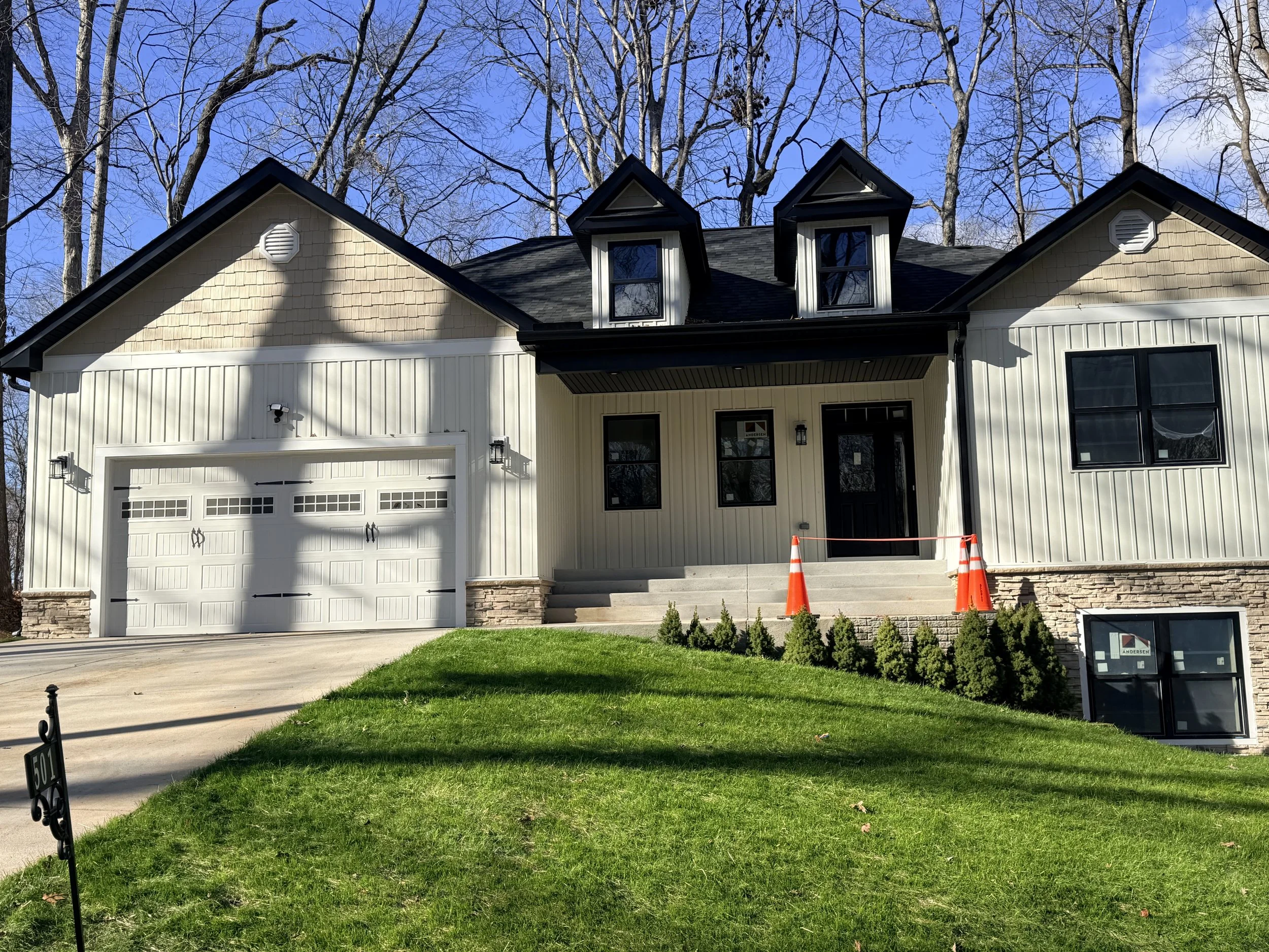 A newly renovated house with a white exterior, black roof, and dormer windows, with a front porch, dual garage, and a green lawn.