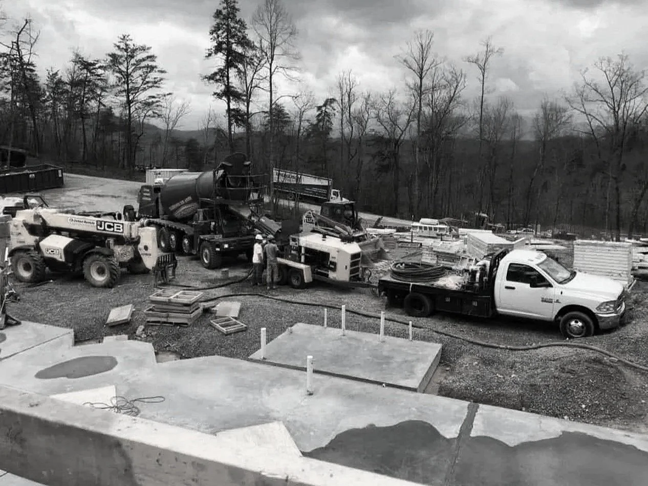 Knoxville Concrete Pumping Construction site with machinery, trucks, and workers, surrounded by trees and overcast sky.