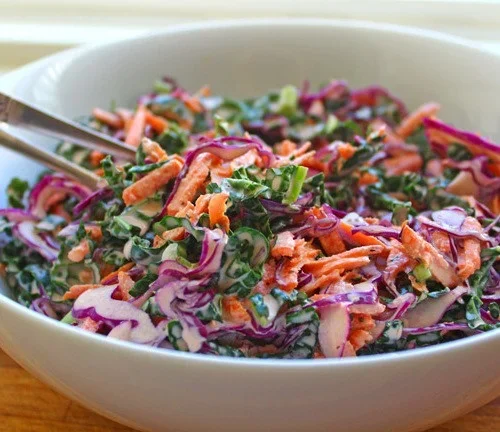 A bowl of colorful shredded cabbage salad with carrots and green onions, served with a fork.
