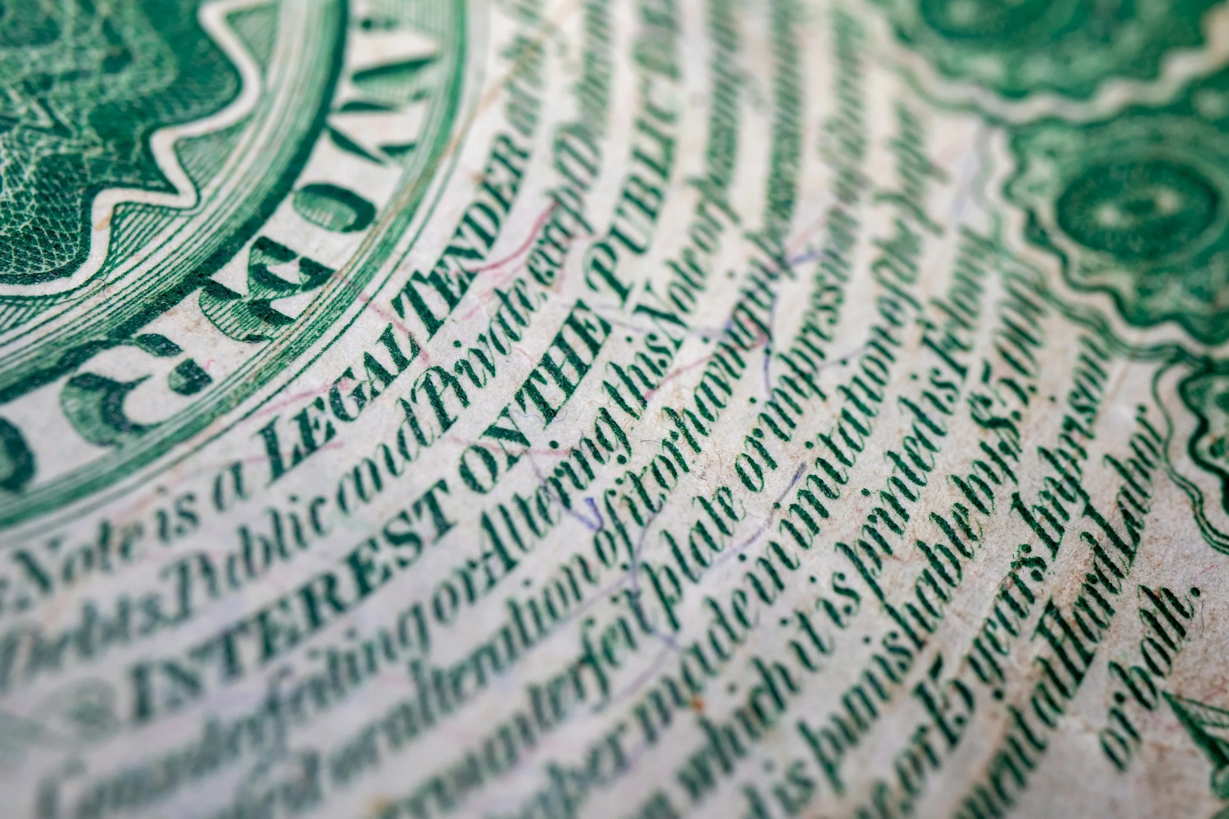 Close-up of a green and white printed paper, likely a banknote or currency, with detailed text and design elements.