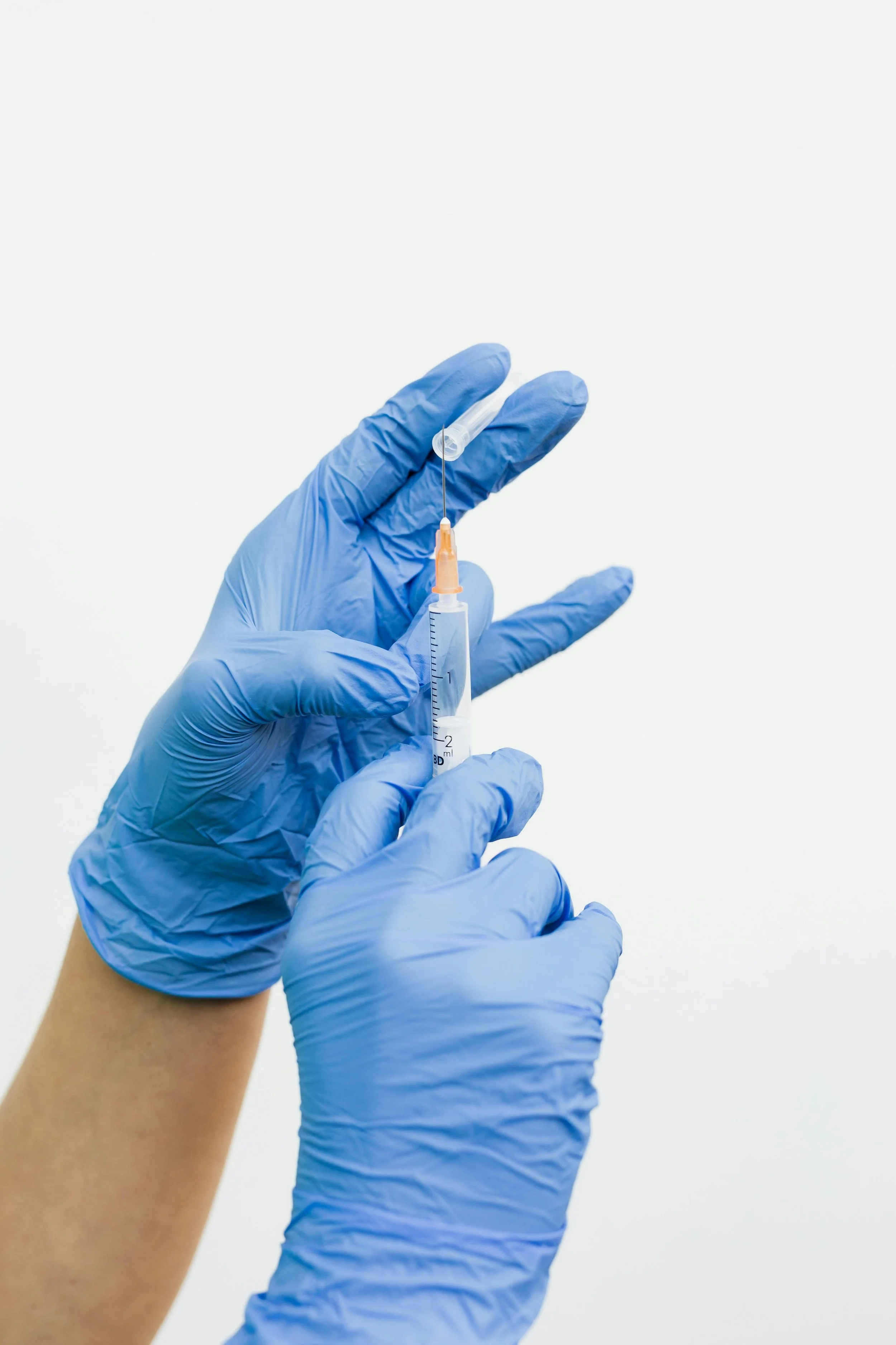 Hands wearing blue gloves prepare a syringe with a needle.