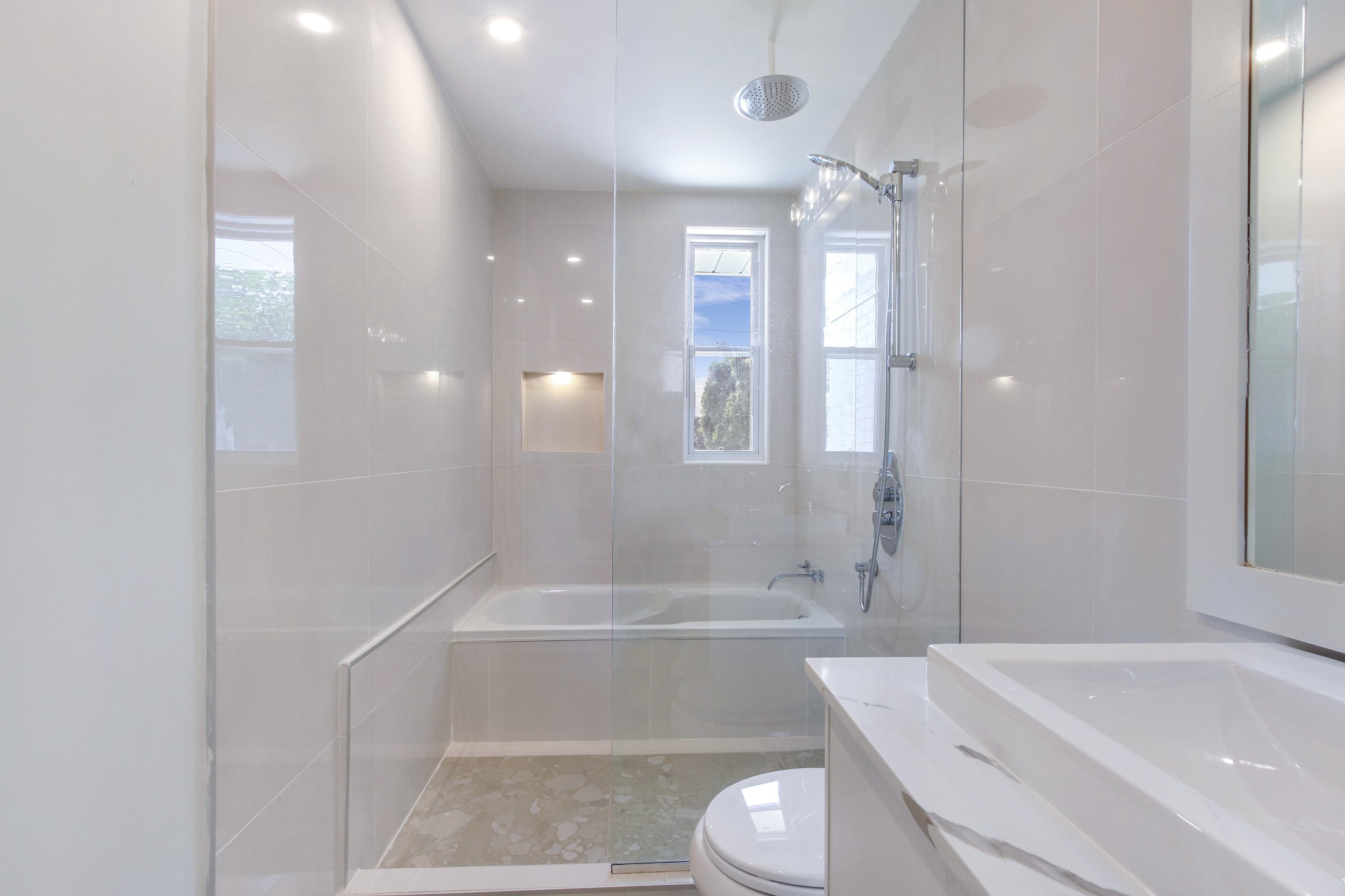 Modern bathroom with bathtub and shower, white tiled walls, window, mirror, and sink.