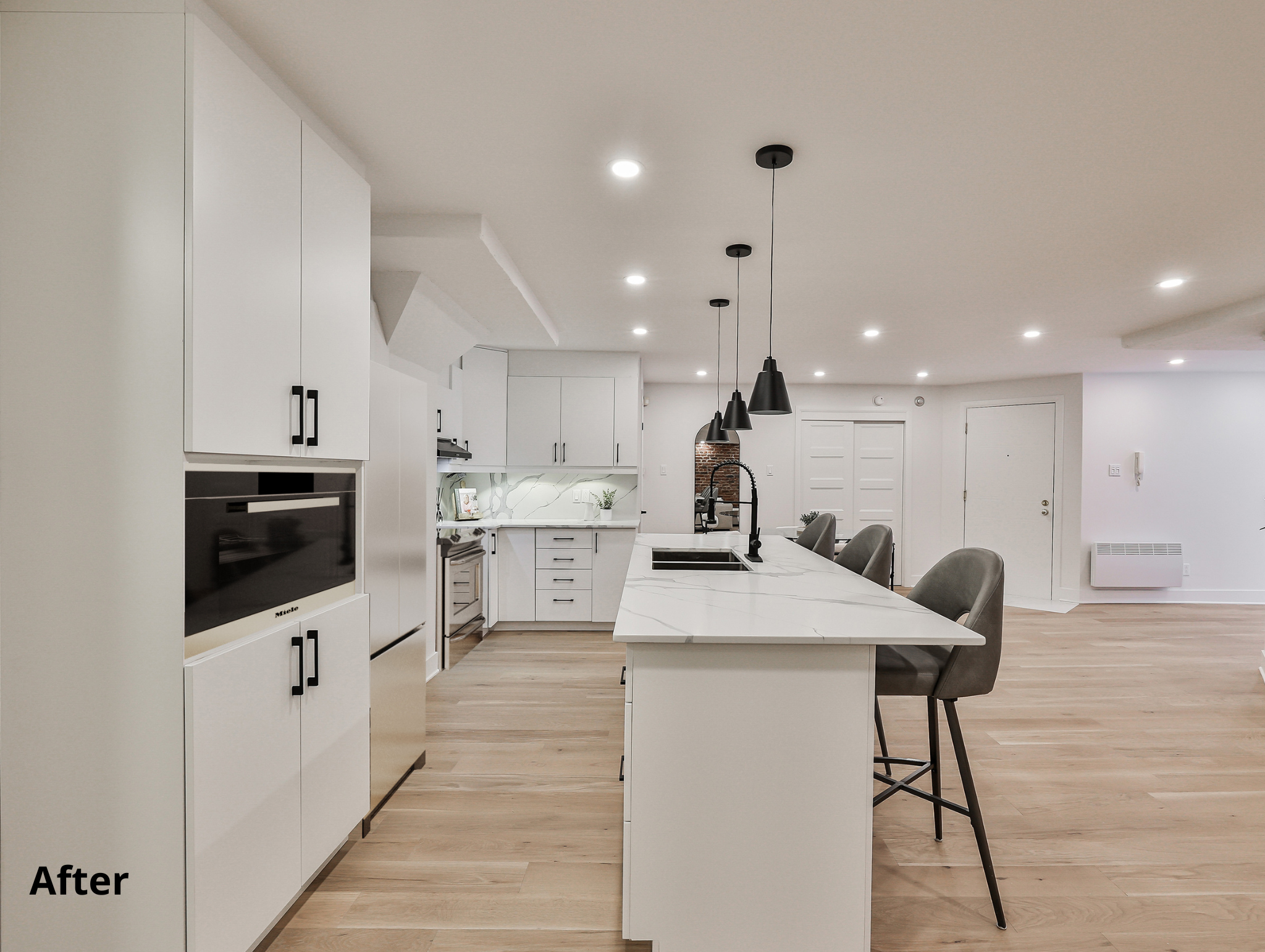 Modern kitchen with white cabinetry, marble island, black pendant lights, and light wood flooring.
