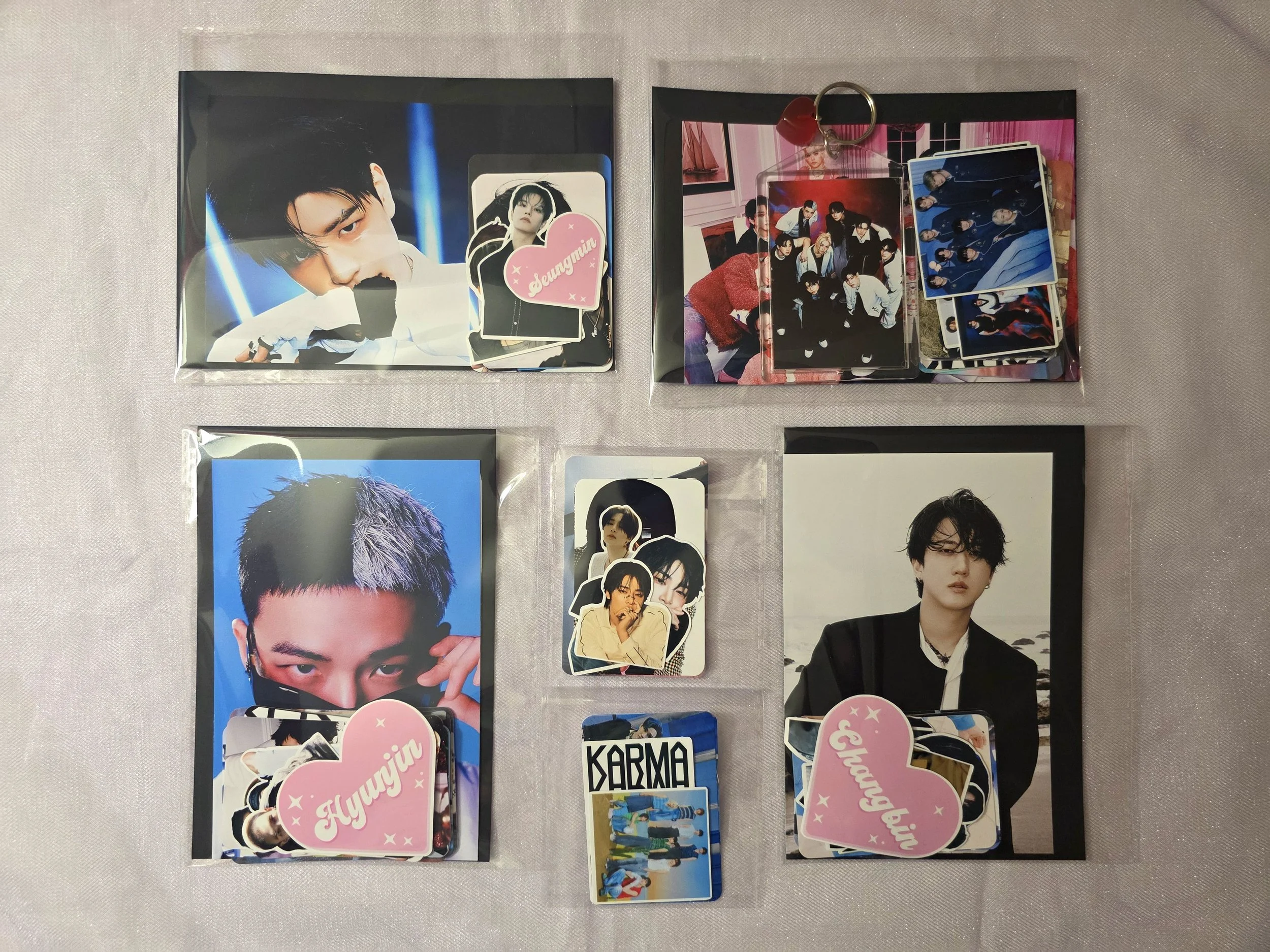 Collection of K-pop photo cards and small photo books featuring male group members, with some cards labeled 'Hyunjin' and 'Bangchan', organized in plastic sleeves and a small ring binder.