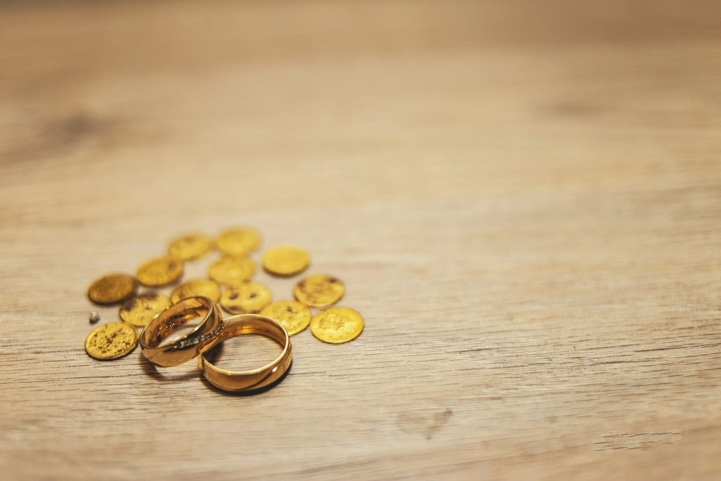 Two gold wedding bands resting on a wooden surface among scattered gold coins.