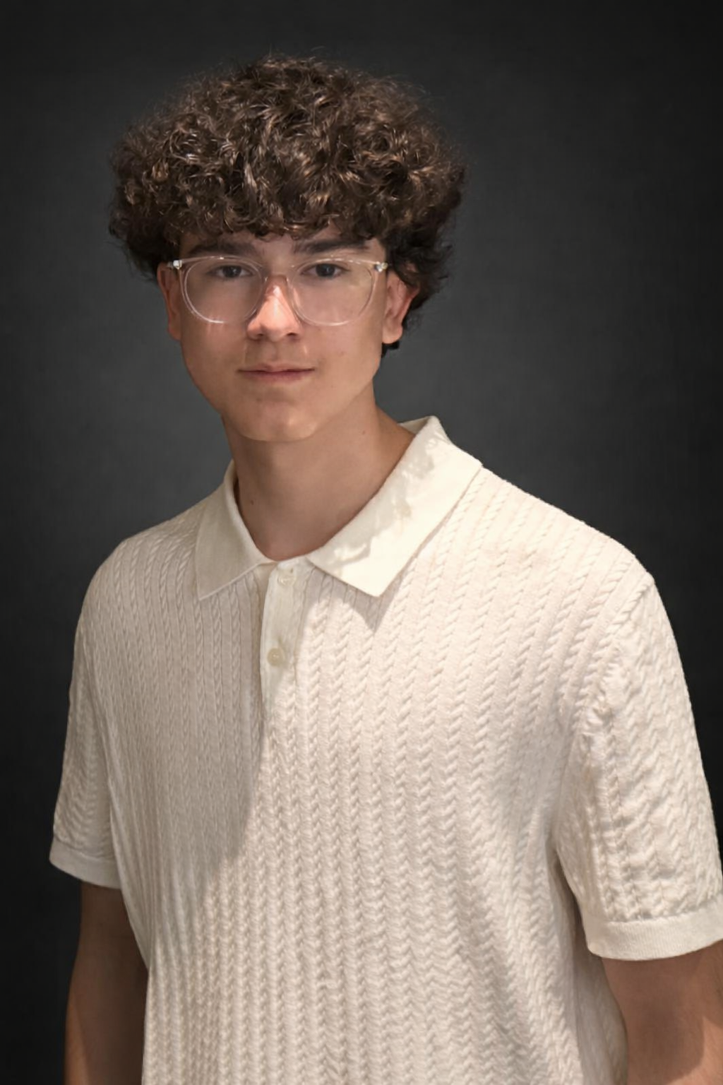 A headshot of Nicolas Miramontes Jr with curly brown hair, wearing clear glasses and a cream-colored textured polo shirt, stands against a dark background.