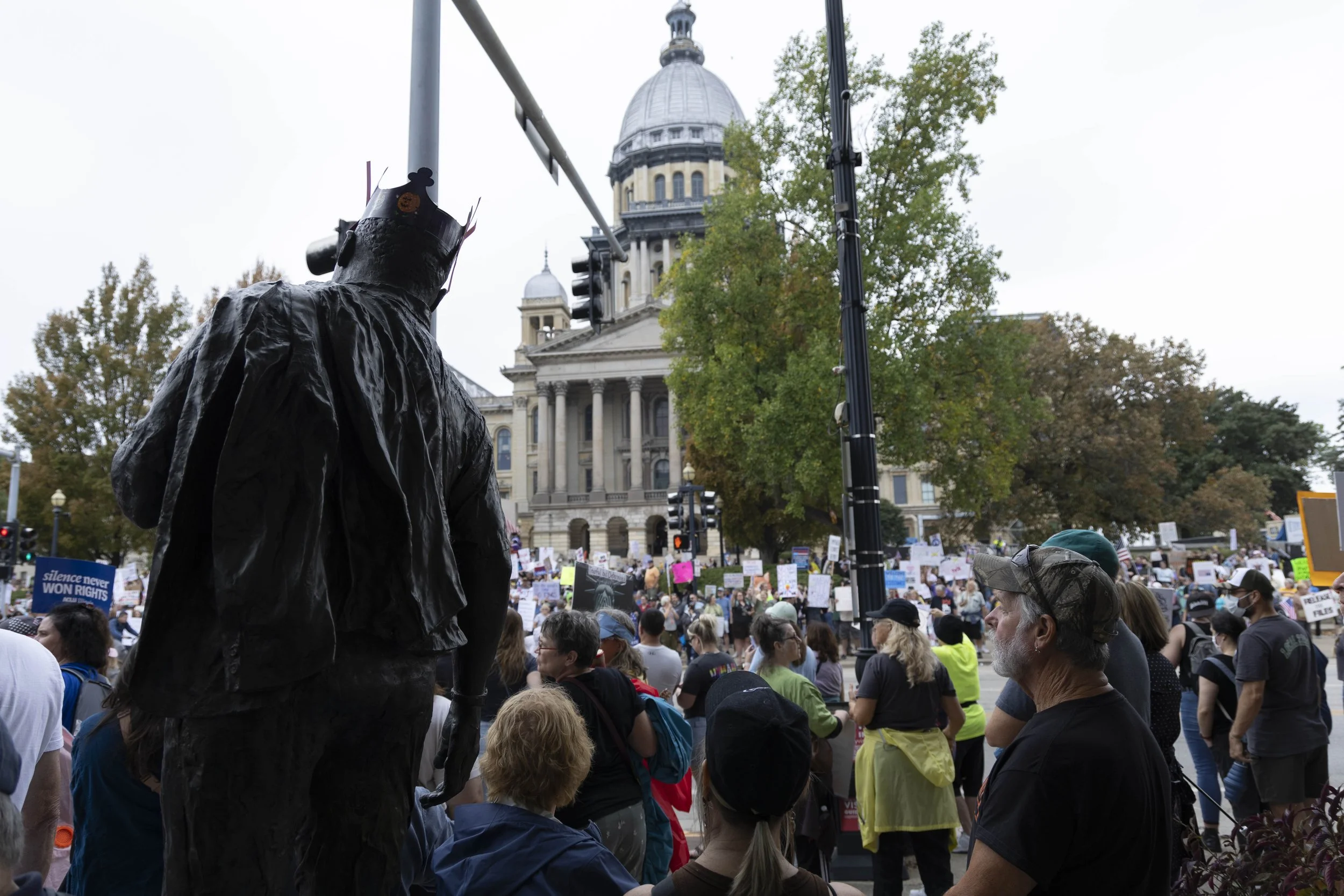 Protesters gather outside the Illinois State Capitol while a Burger King Crown sits on a Martin Luther King Jr. statue at the No Kings protest Oct. 18, 2025 in Springfield, Illinois