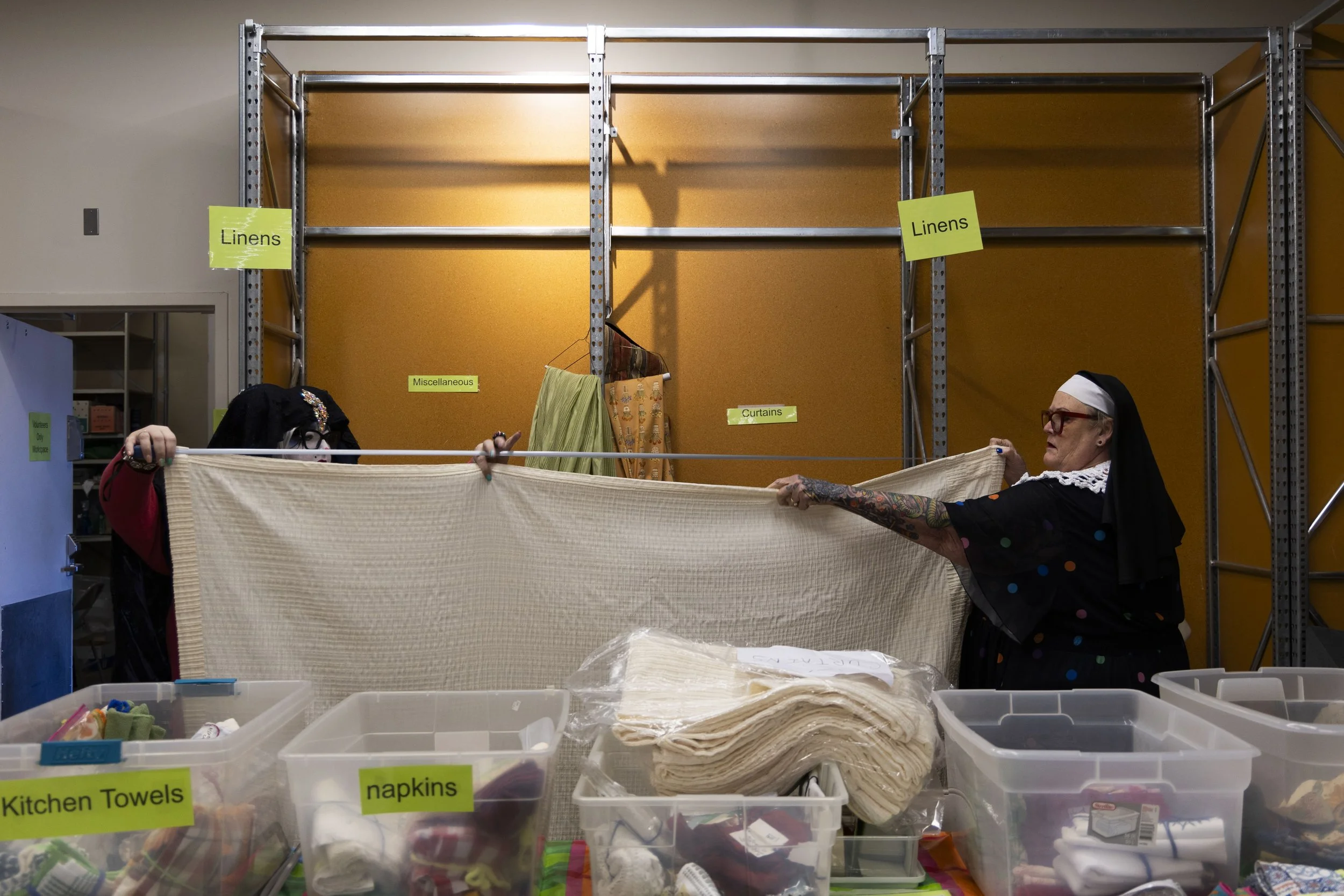 Maggie Degen (Sister Gay Bitch Milkshake) holds up a blanket with Christina Ivey (Sister Benadetta) to measure how long it is to determine what price it should be sold at the Hunger Sale May 1, 2026 at the University Mall in Carbondale, Illinois. 