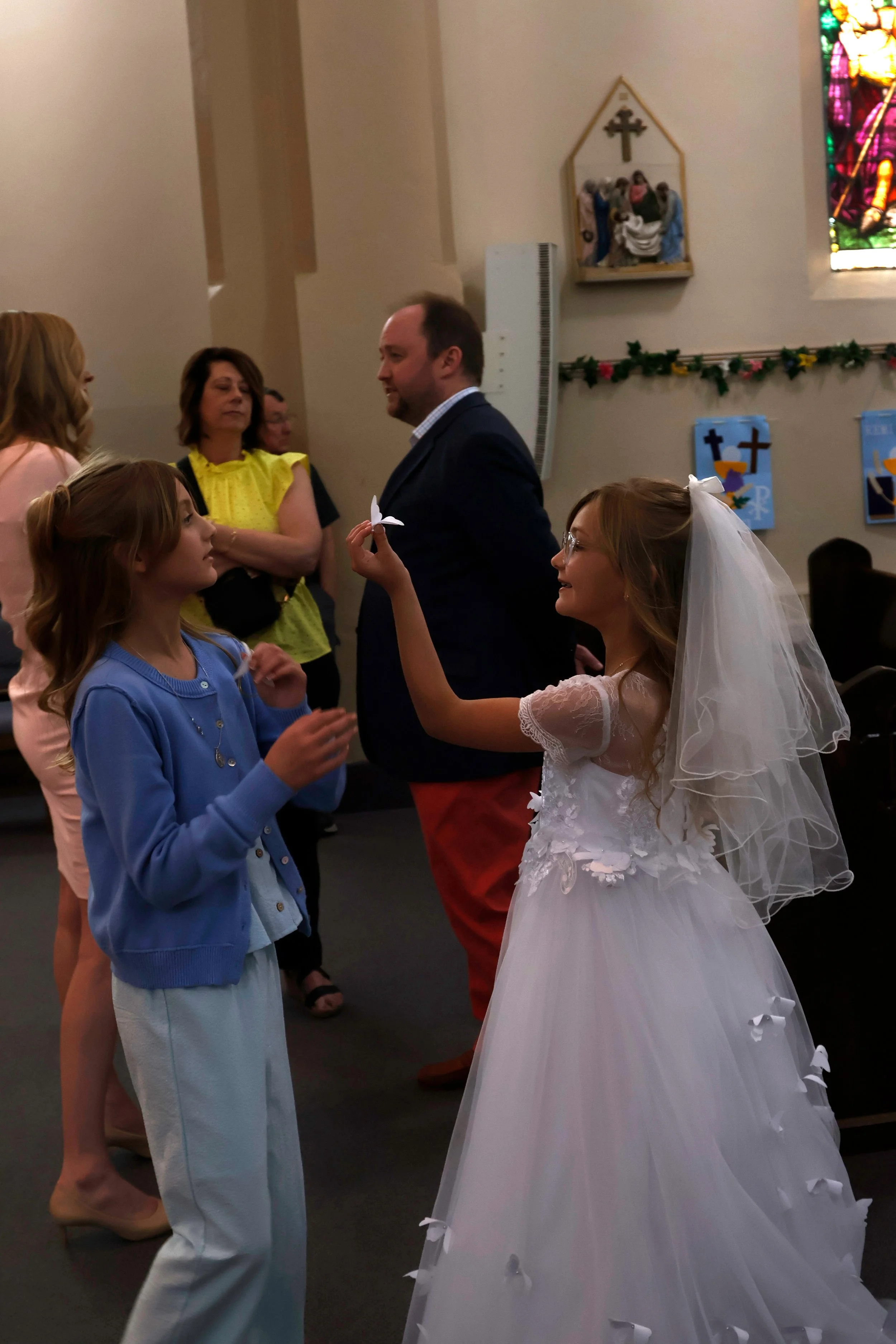Marcella Haney shows her sister Lydia Haney a butterfly that fell off her dress April 11, 2026 at St. Andrew’s Catholic Church in Murphysboro, Illinois. 