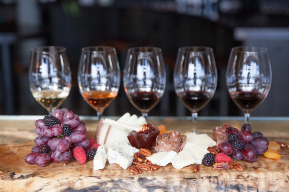 Cheese platter with grapes, berries, nuts, and wine glasses in the background.