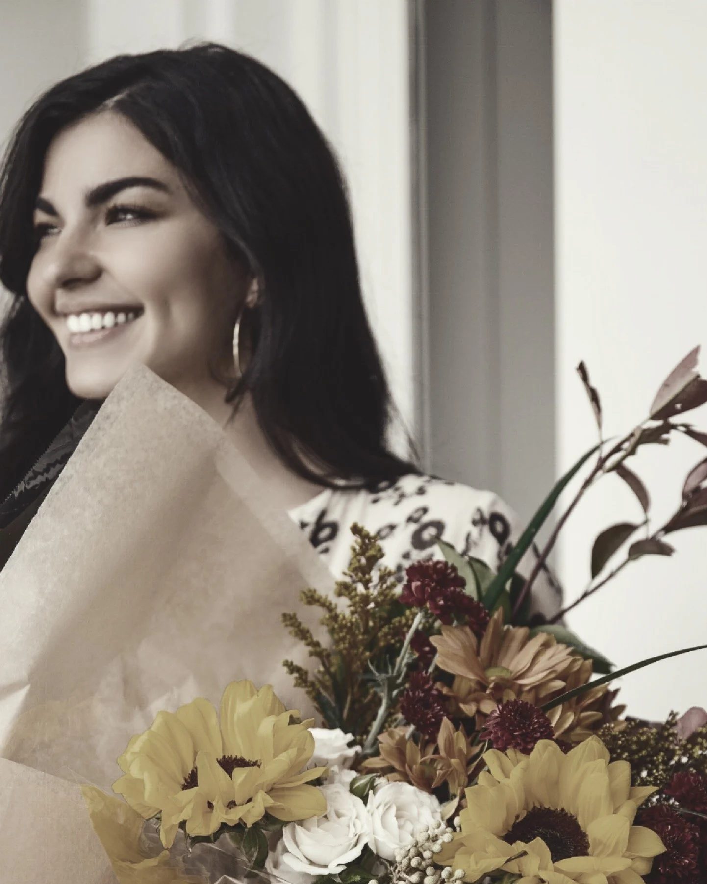 A woman with long black hair holding a bouquet of flowers and smiling
