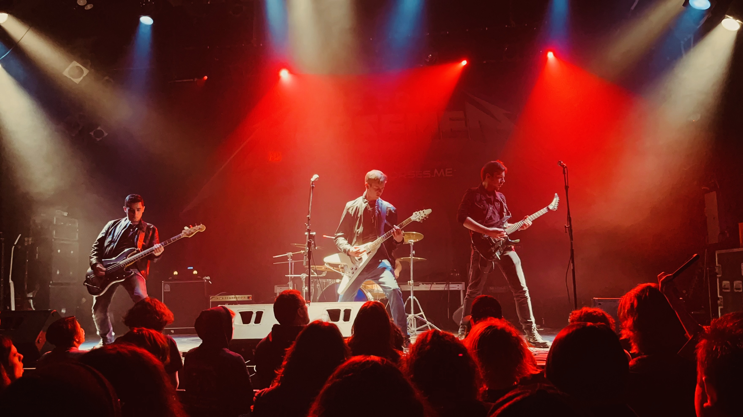 A band of four musicians, Mainline, performing on stage at a concert, with colorful stage lights shining down on them and an audience in the foreground.