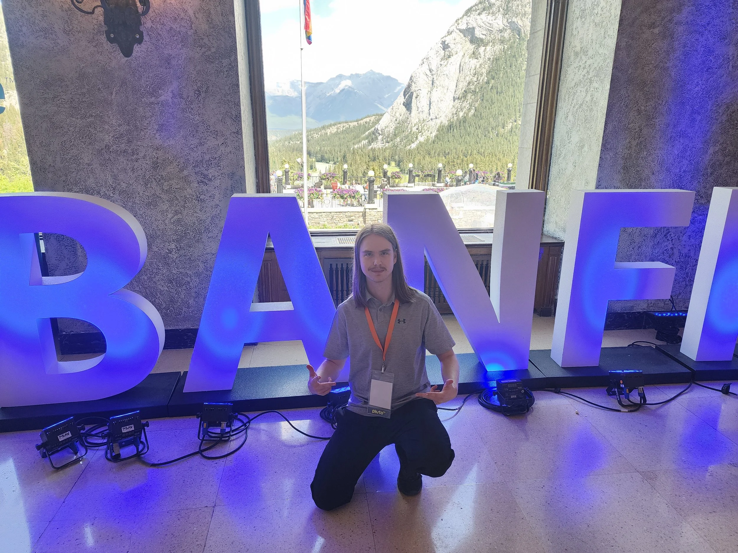 Kade Stevens kneeling in front of large illuminated letters spelling 'BANFF' at the Banff World Media Festival.