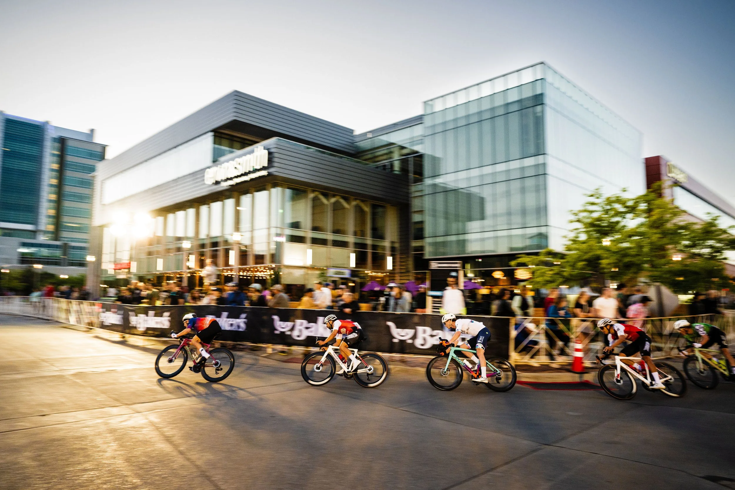 Group of cyclists racing in the Aksarben Tirc Race in front of Ervin & Smith. The image is at sun set.