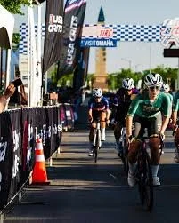 Criterium racers, racing through the streets of Aksarben. You see the race barriers and the finish line.