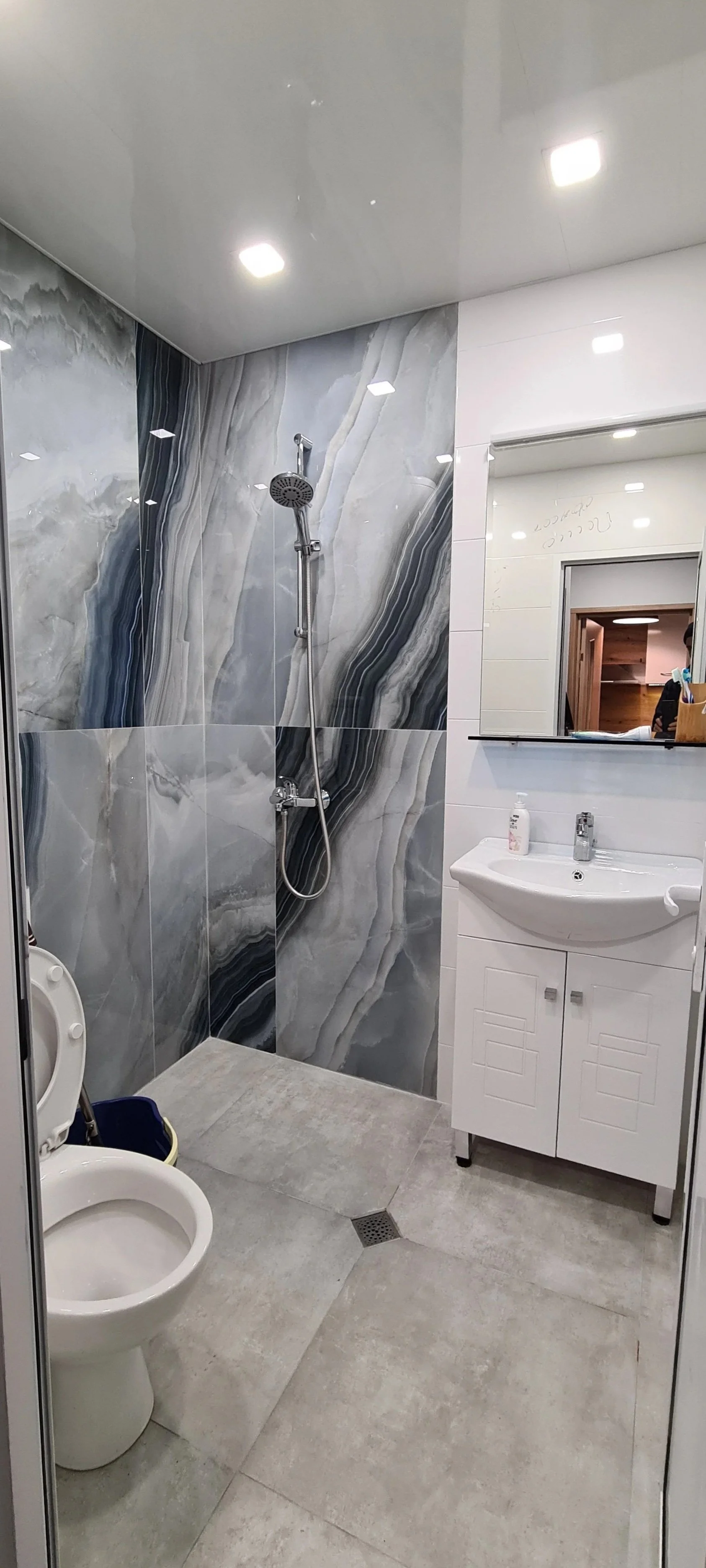 Bathroom with gray marble shower wall, white vanity with a mirror, and a toilet.