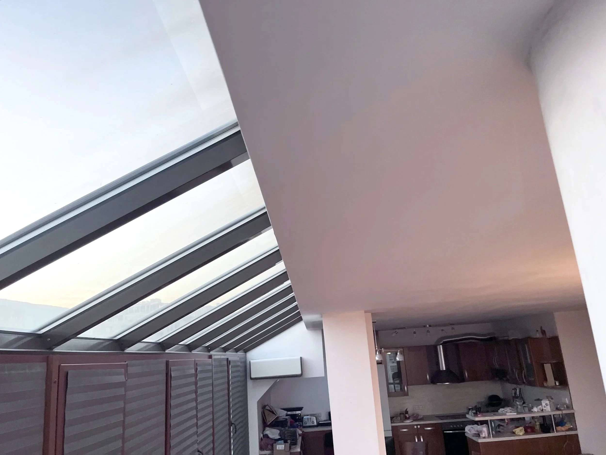 Photo of an indoor space with large glass windows, white ceiling, and a kitchen area with wooden cabinets.