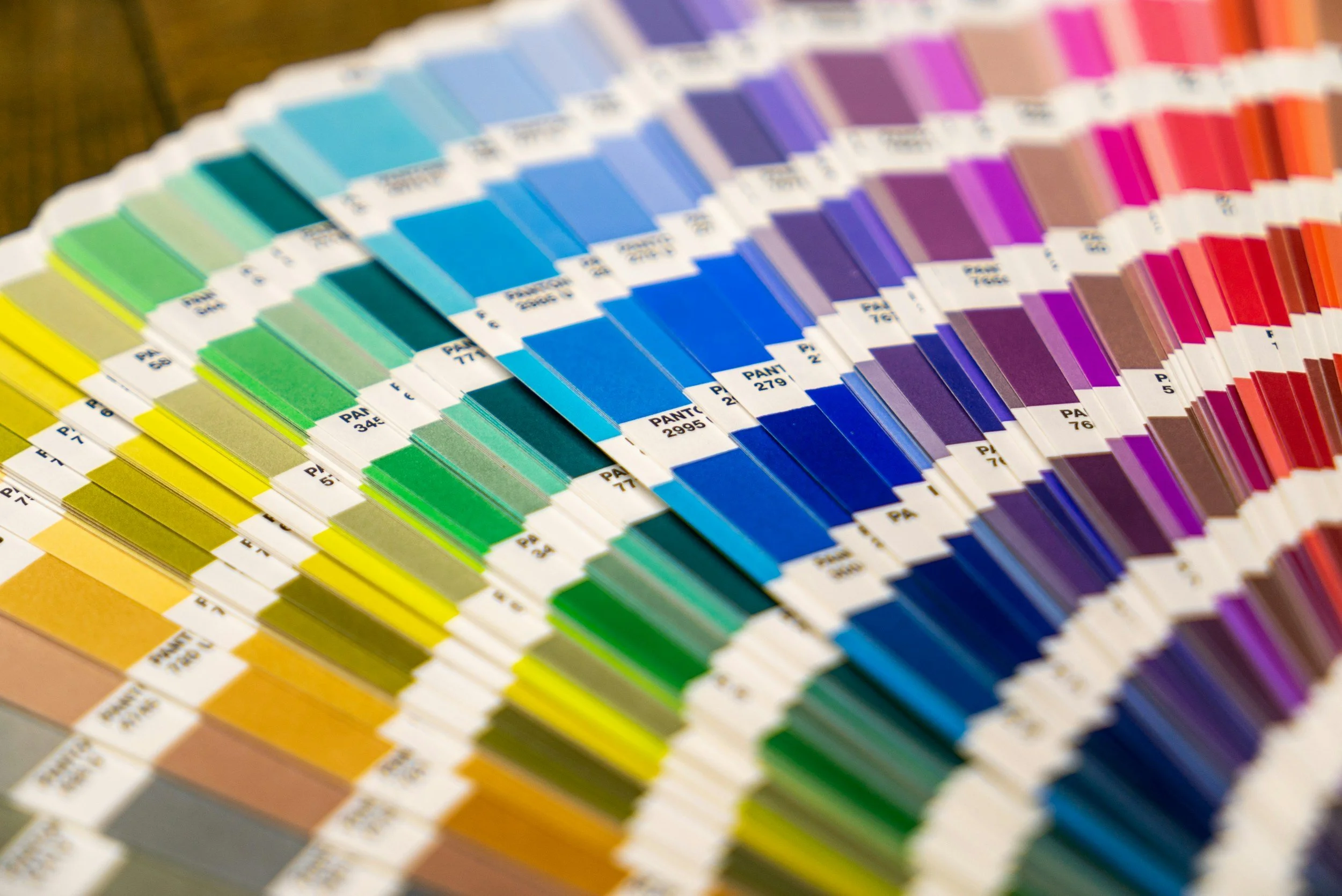 A fan deck of paint color swatches arranged in a rainbow gradient, from yellow and green to blue, purple, pink, red, and brown.