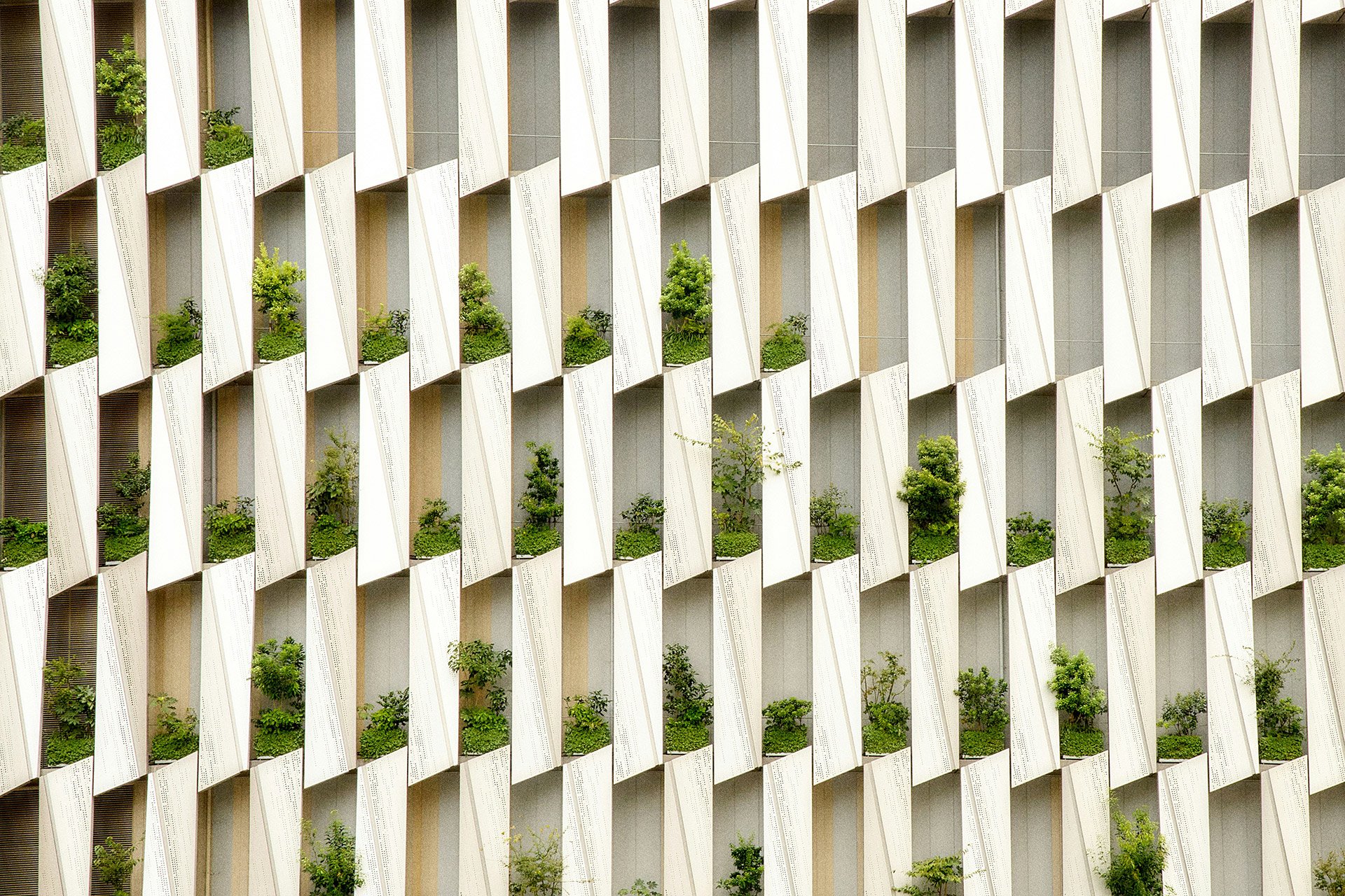 Façade d'un bâtiment moderne avec des balcons en saillie et des plantes vertes dans chaque balcon.