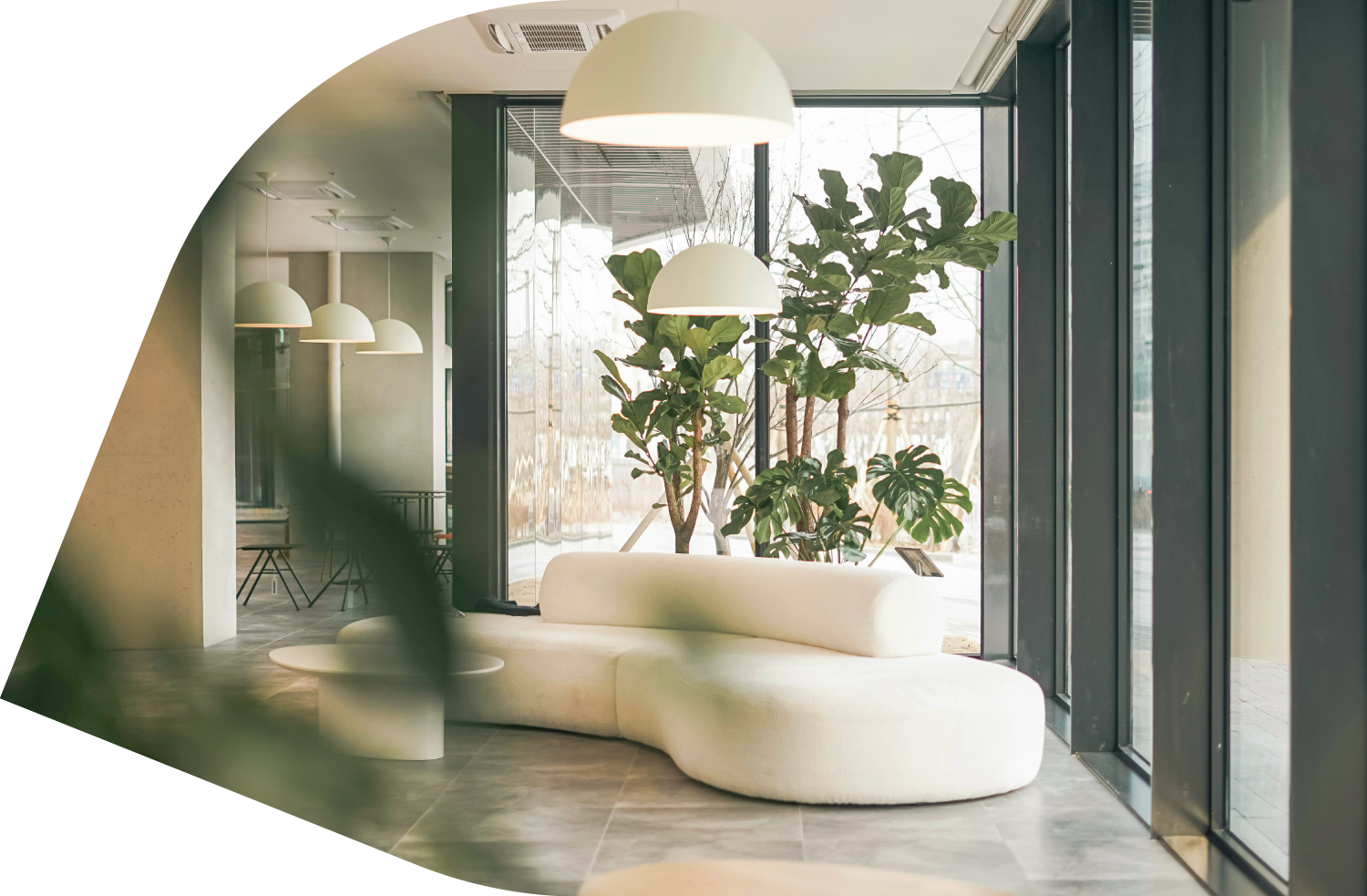 Intérieur moderne avec un canapé blanc incurvé, plantes vertes près de grandes fenêtres, lampes suspendues blanches au plafond