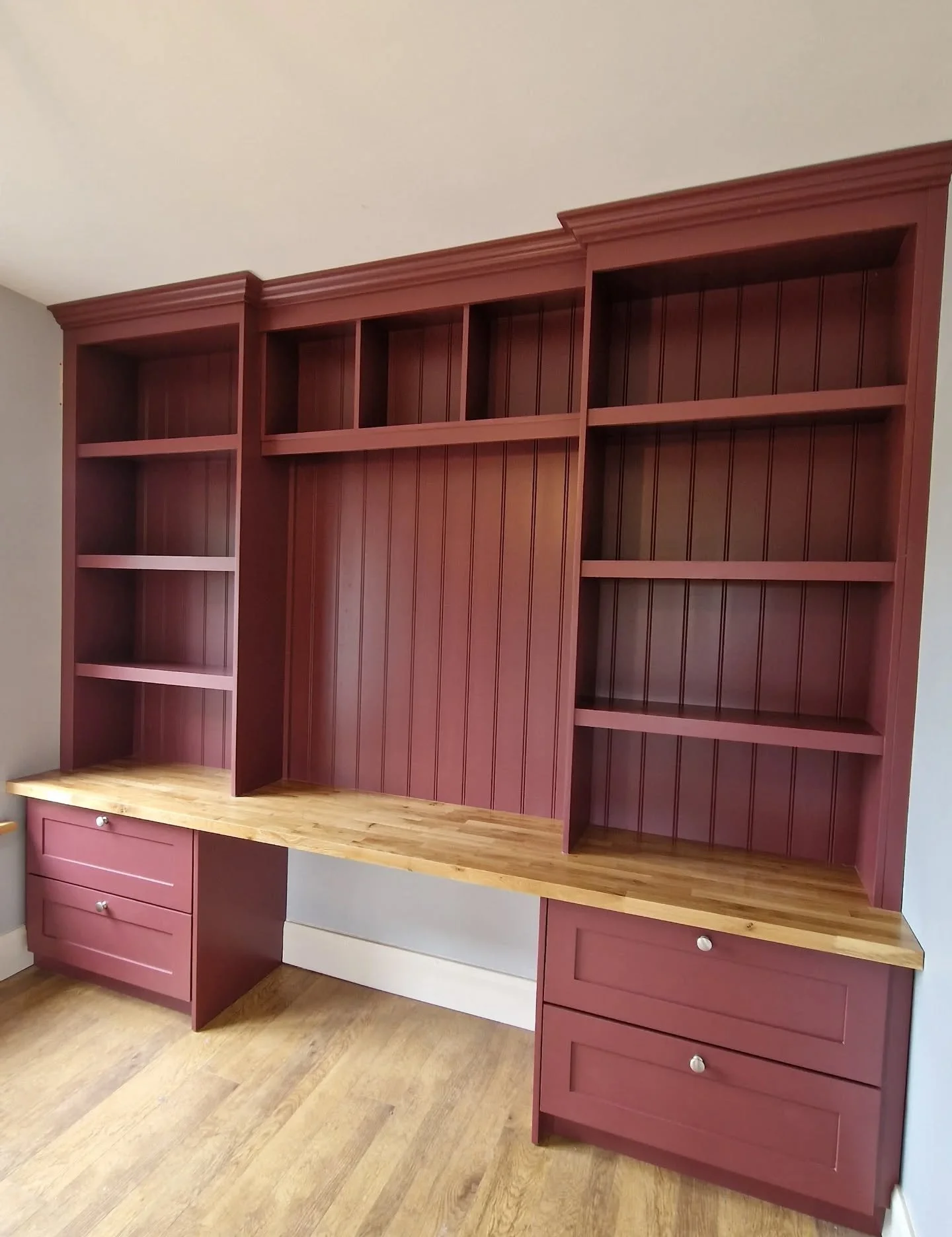 Brown built-in bookshelf with open shelves and a wooden countertop in a room with hardwood floors.
