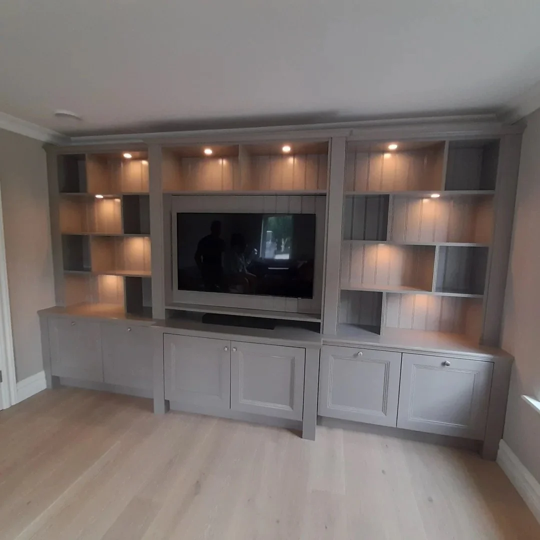 Empty built-in wall entertainment center with shelves and cabinets, with a mounted TV and warm lighting