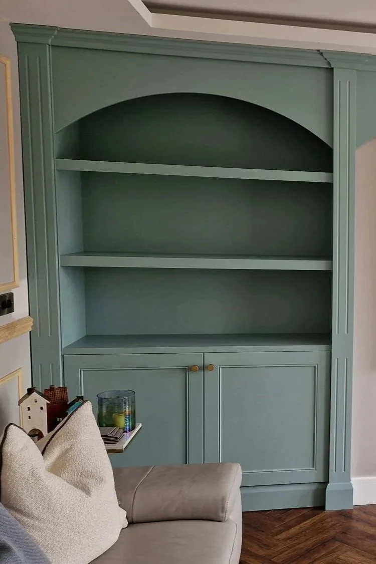 A large, light blue wooden bookshelf with four open shelves and two closed cabinets below, located in a living room corner.