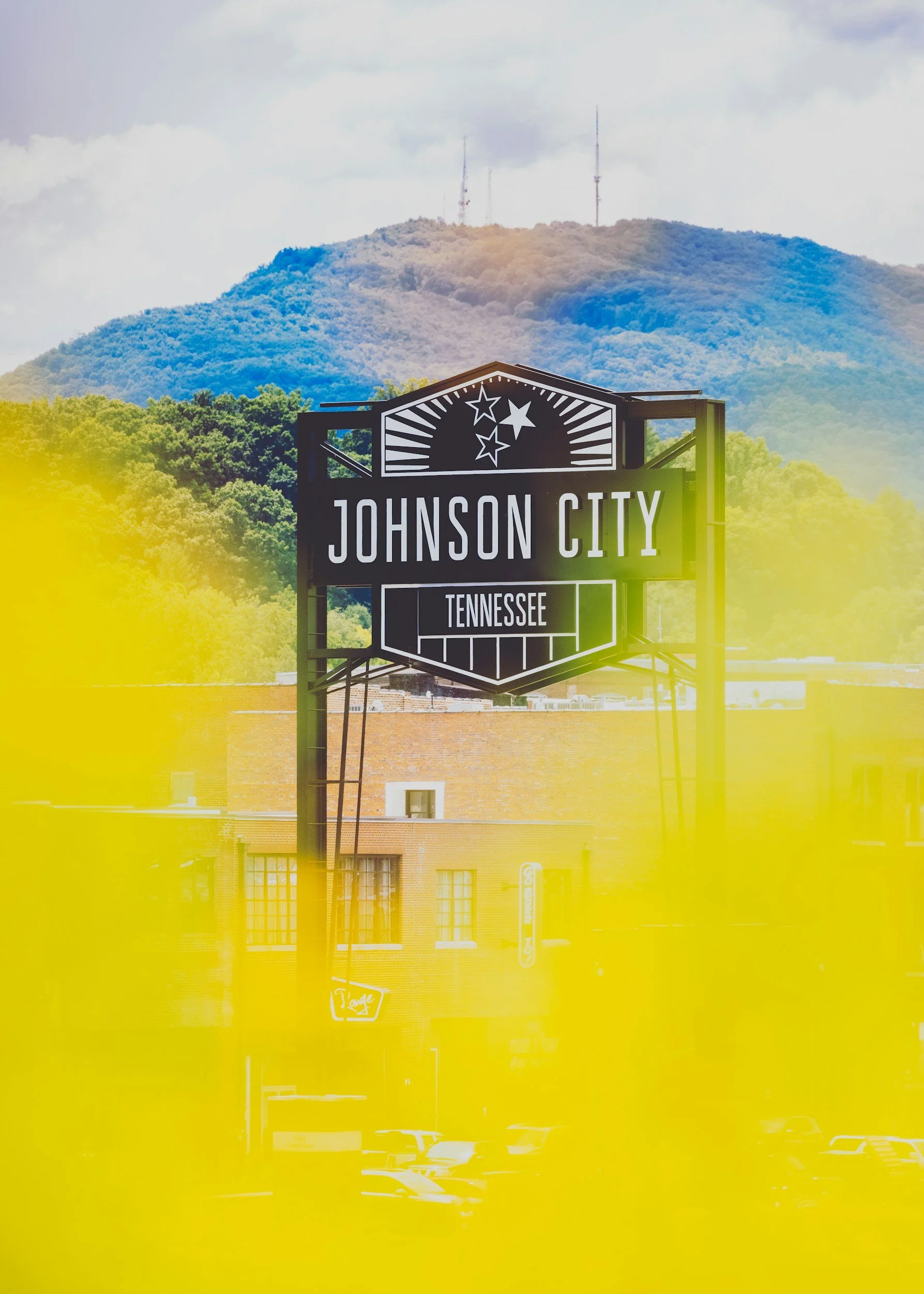 Sign for Johnson City, Tennessee, with a mountain and radio antennas in the background, partially obscured by yellow glare.