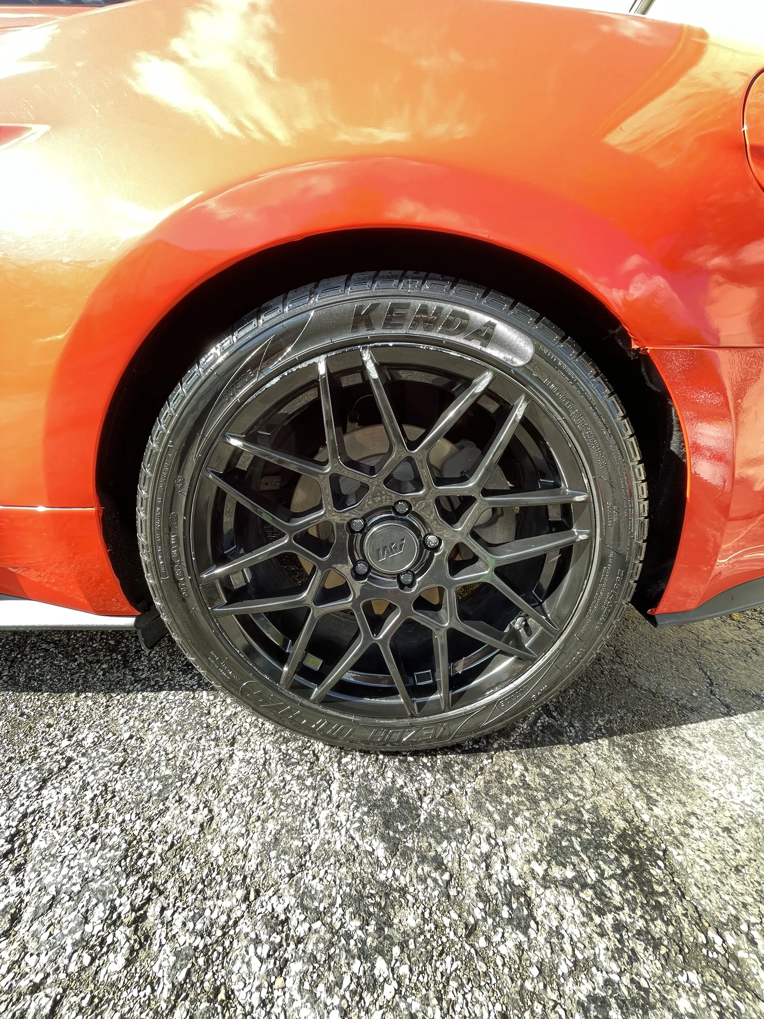 Close-up of a black aftermarket car wheel with Kenda tire on a red sports car parked on asphalt.