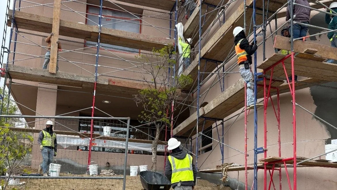 Construction workers in safety vests and helmets working on scaffolding around a multi-story building under construction.