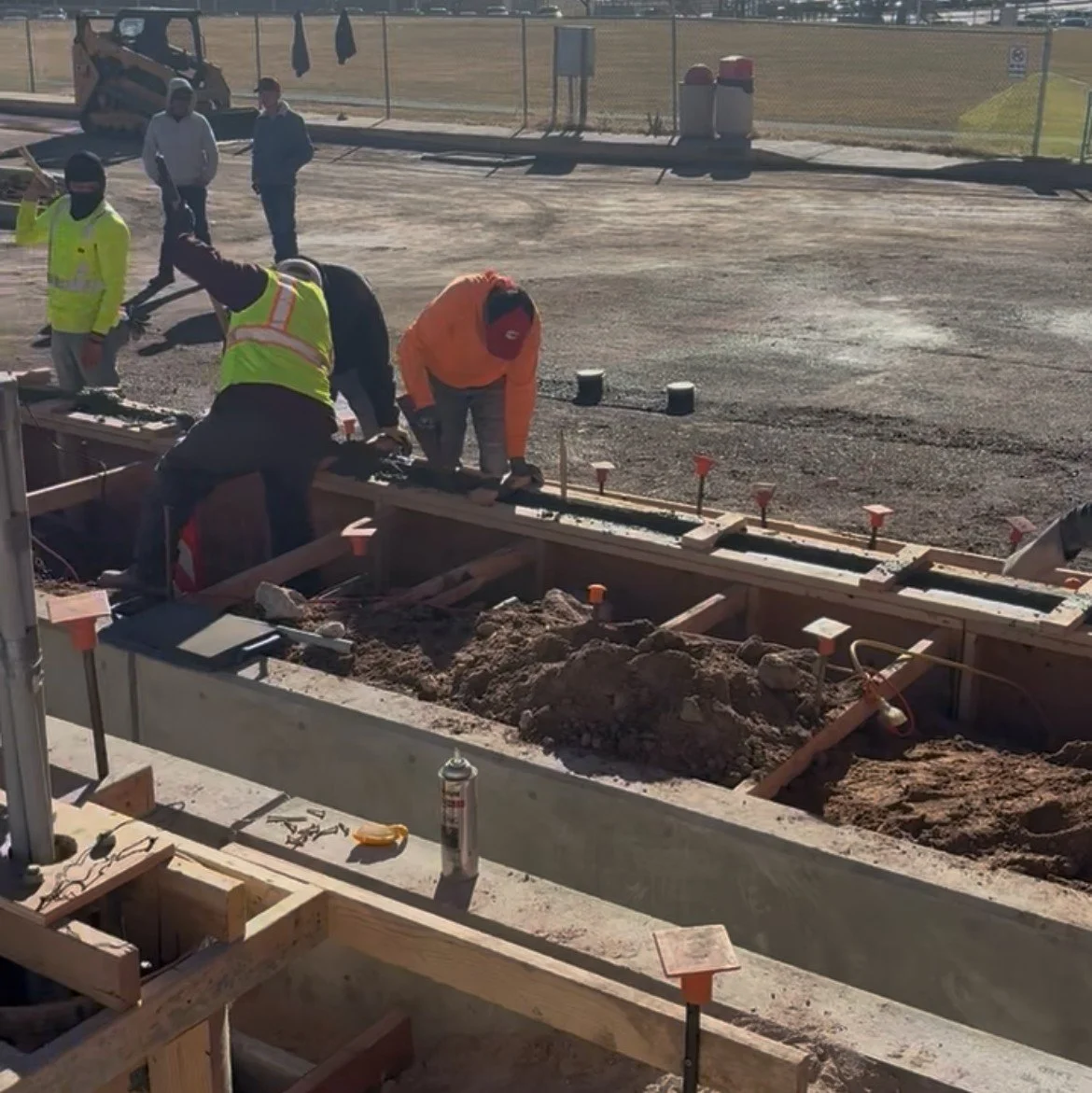 Construction workers building a concrete sidewalk or foundation at a construction site, with some workers inspecting and working on the structure