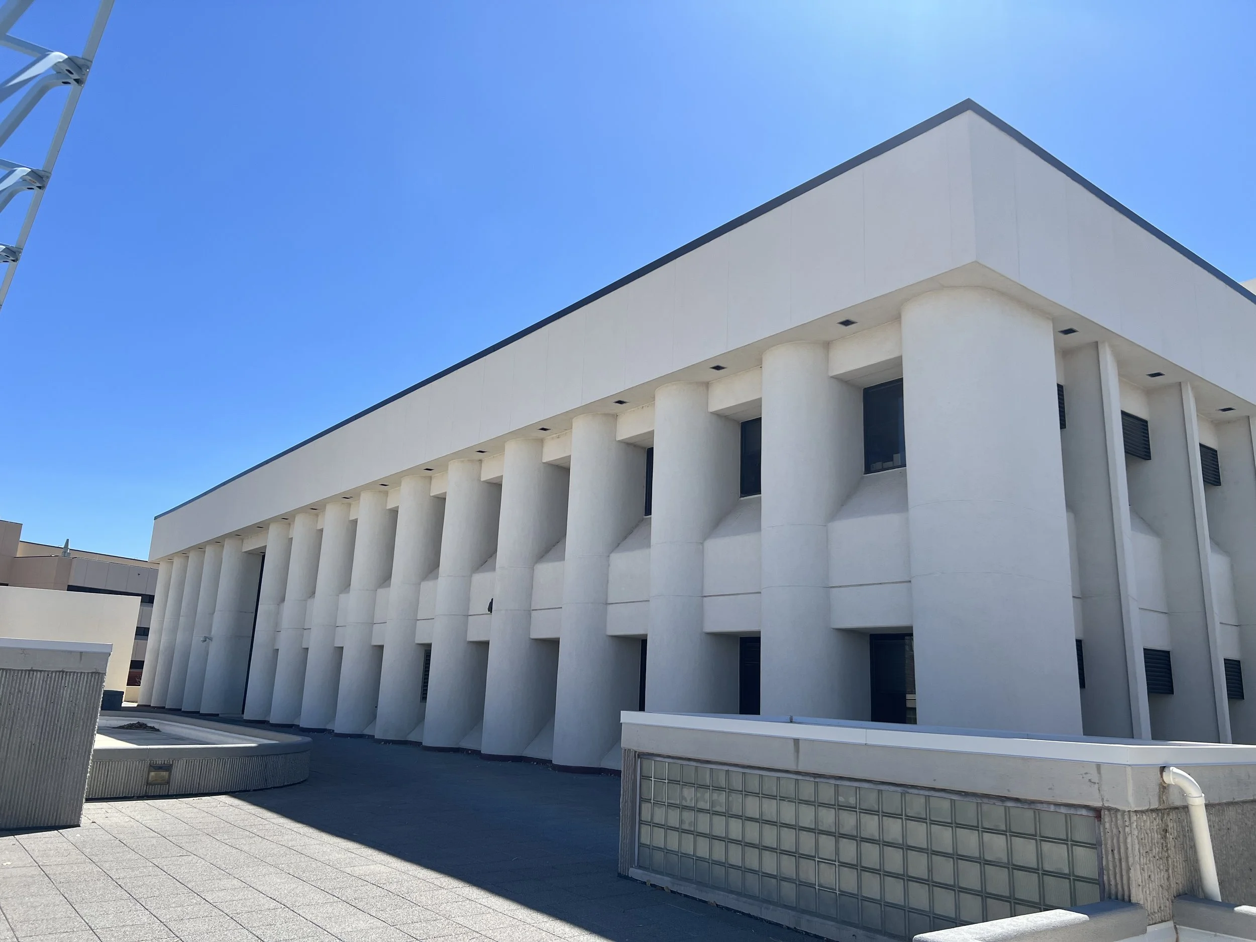 Modern white building with a flat roof and vertical concrete columns, against a clear blue sky.