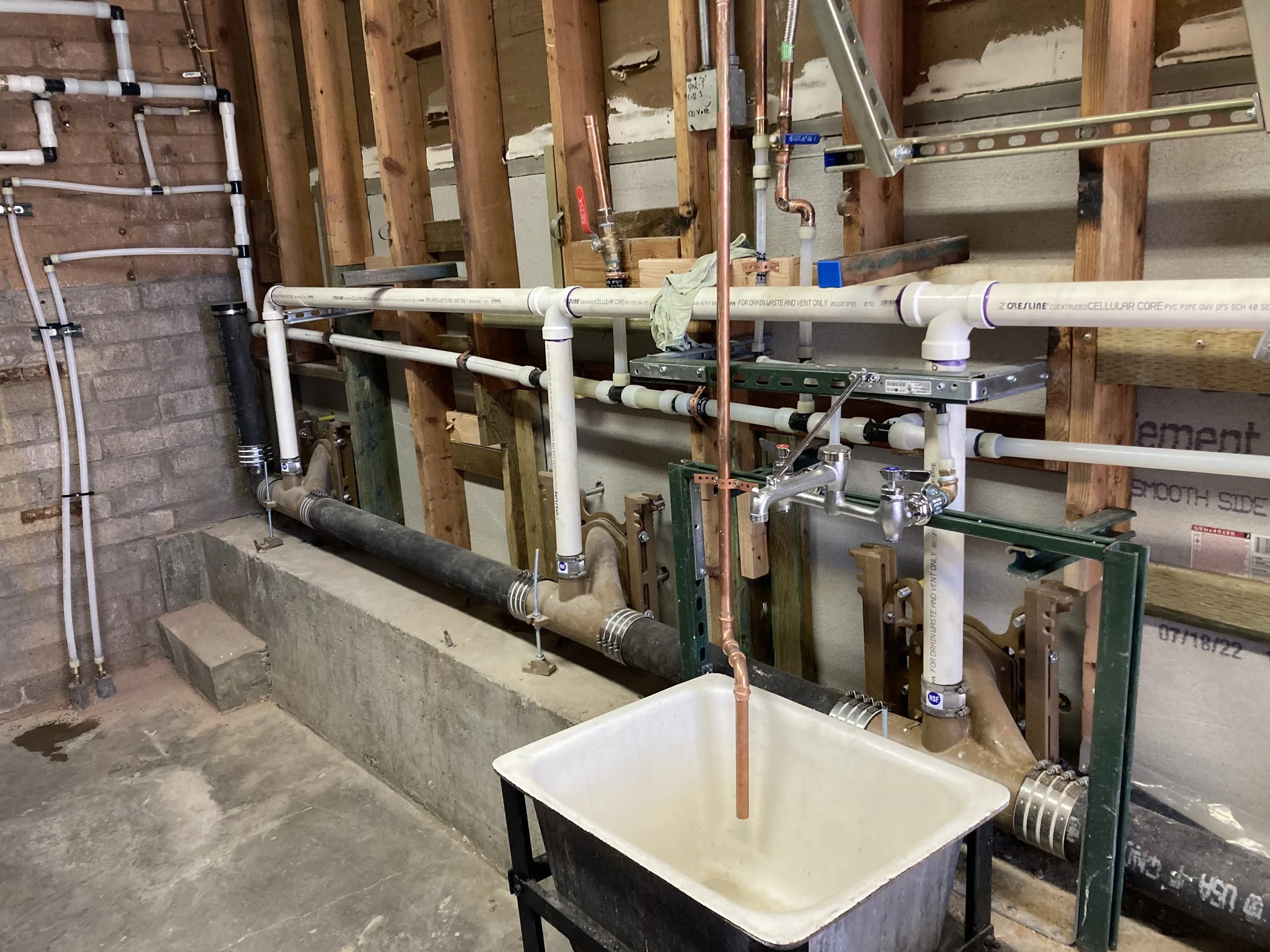 Under construction plumbing system with white PVC pipes, copper pipes, and fittings installed on a wooden framing in a building interior.