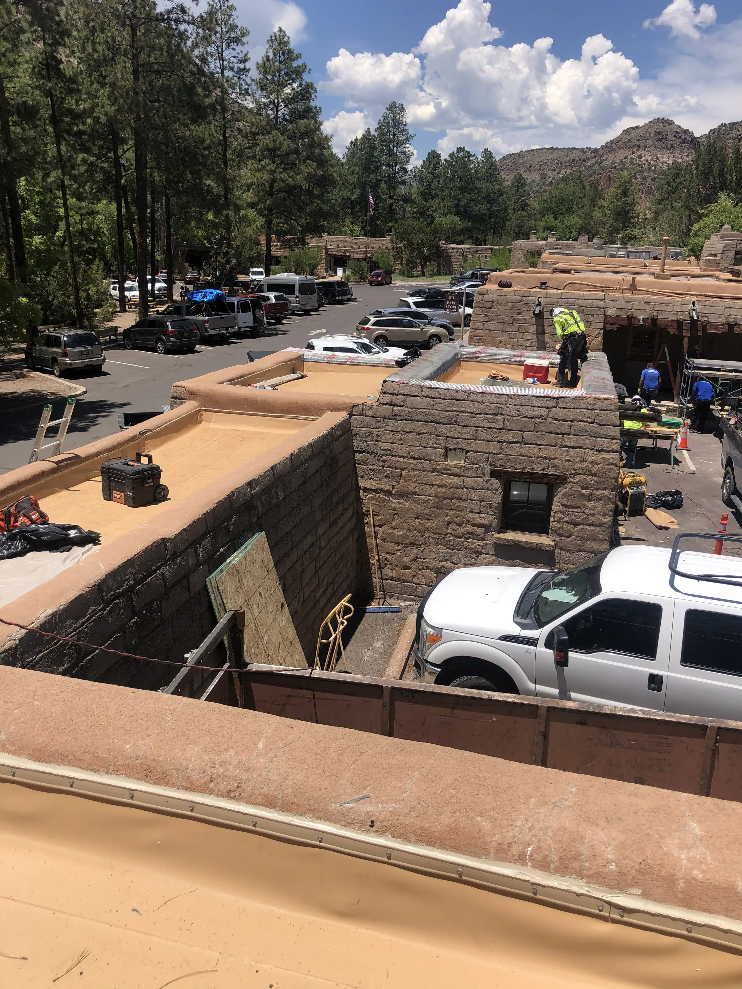 Construction workers working on the roof of a building with a view of a parking lot, trees, and mountains in the background.