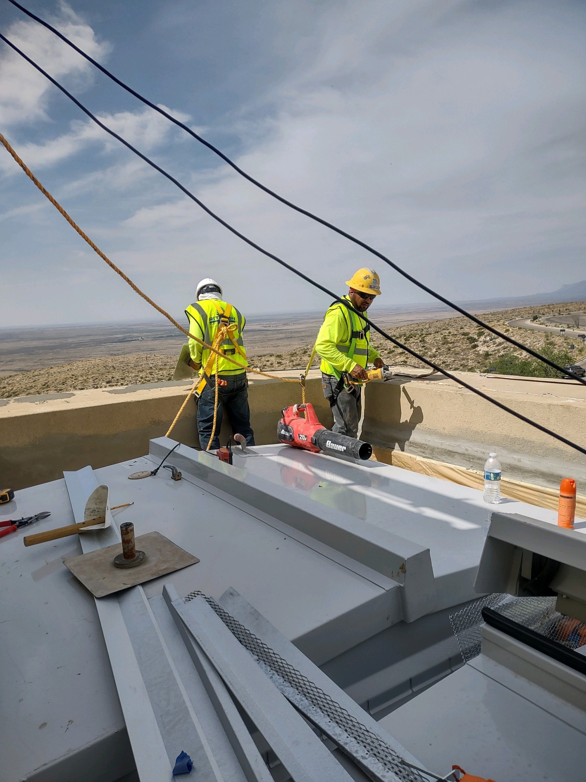 Construction workers in safety gear working on a high-rise building, with a desert landscape and road visible in the background.
