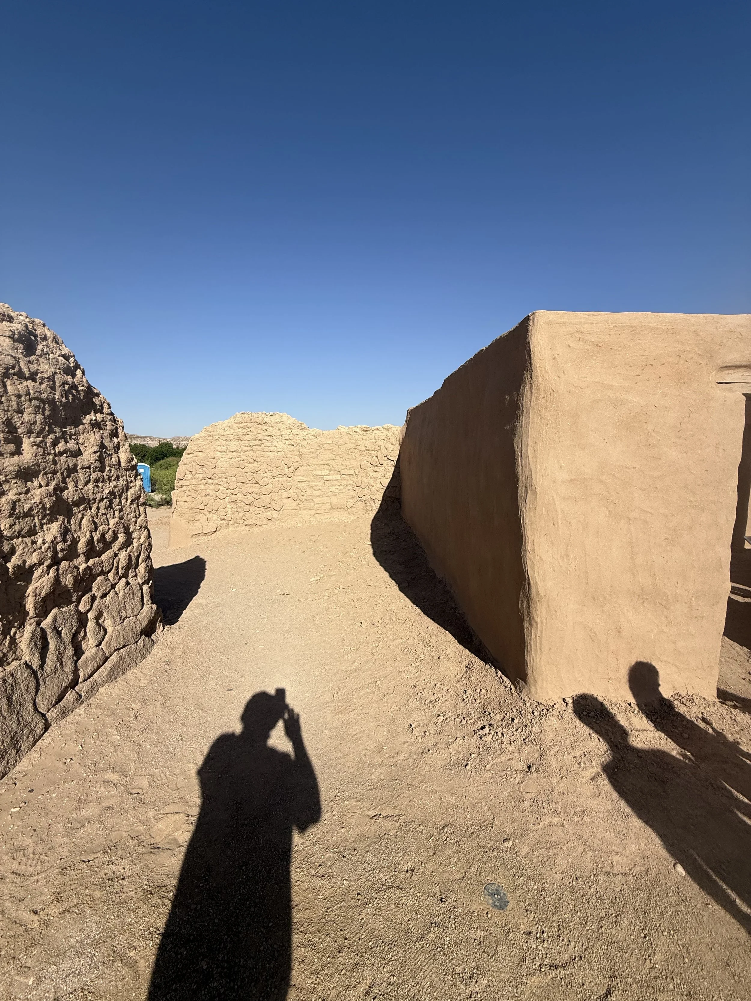 Ancient ruins with stone walls and large clay structures under a clear blue sky.
