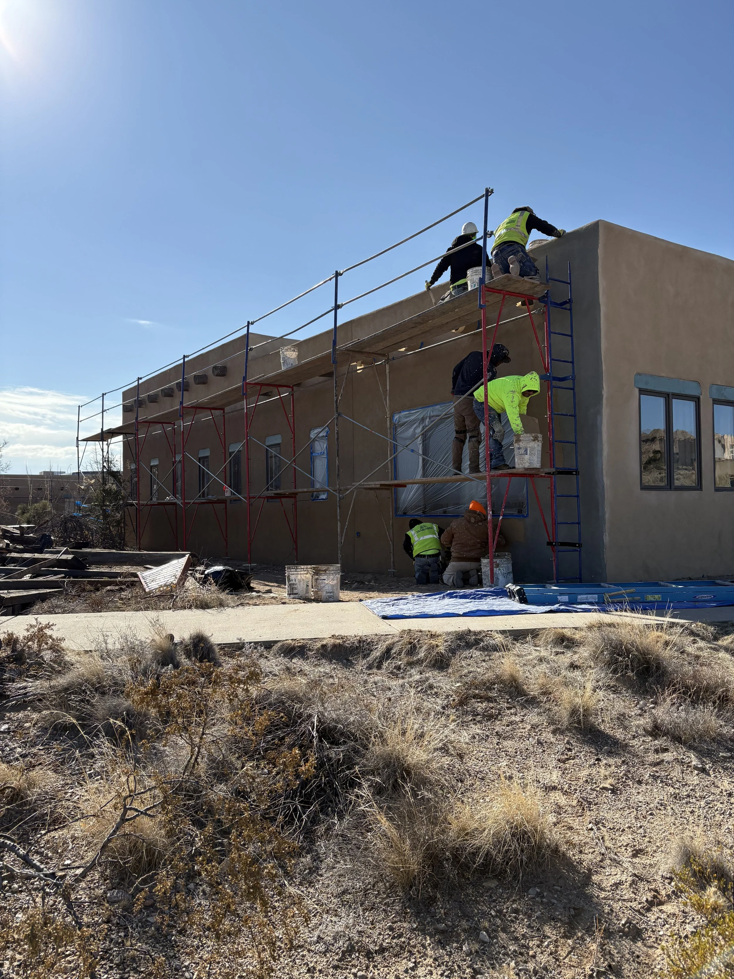 Construction workers building a flat-roofed beige building with scaffolding underneath a clear blue sky.