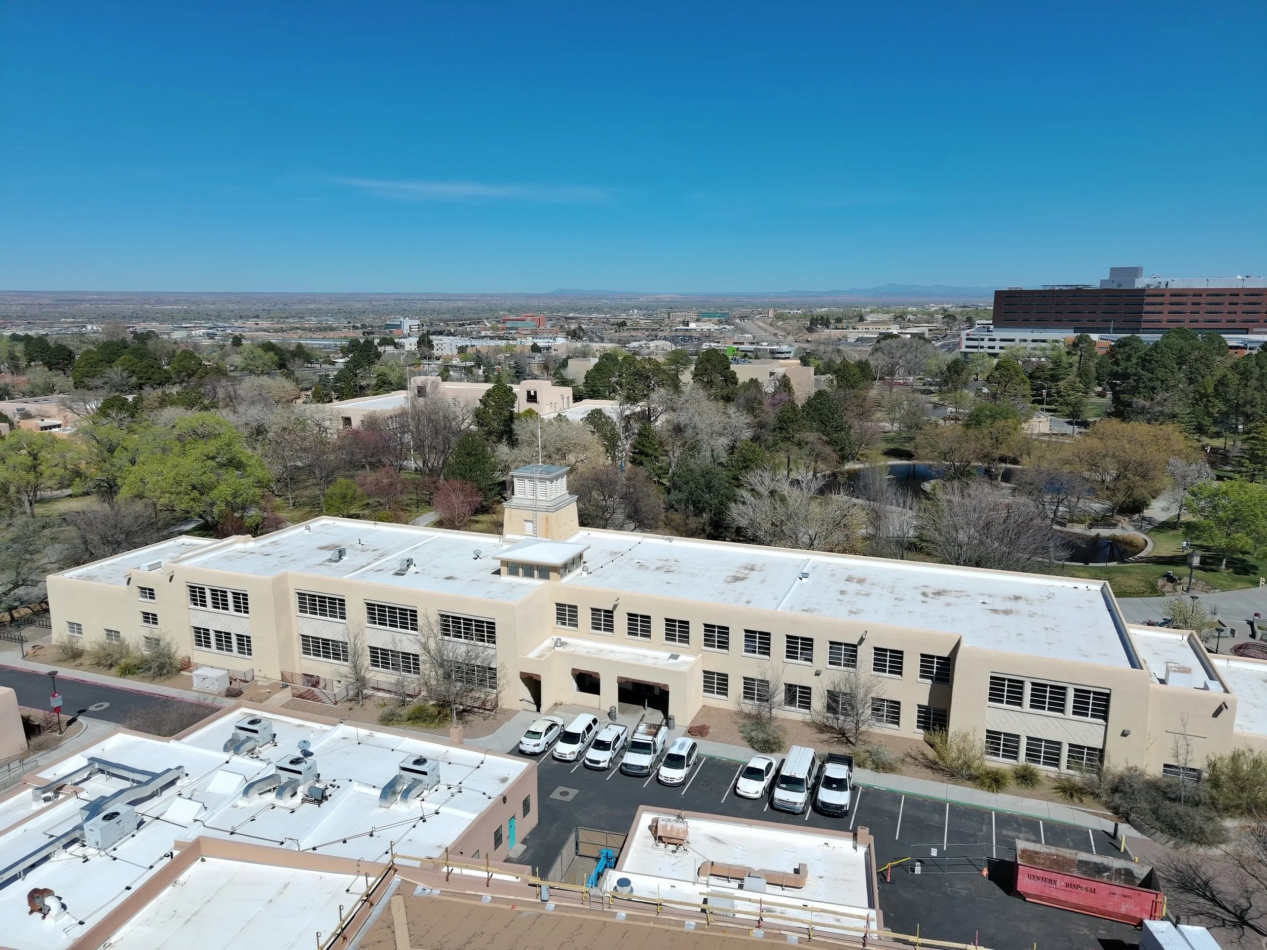 A cityscape with buildings, trees, parking lots, and a clear blue sky in the background.