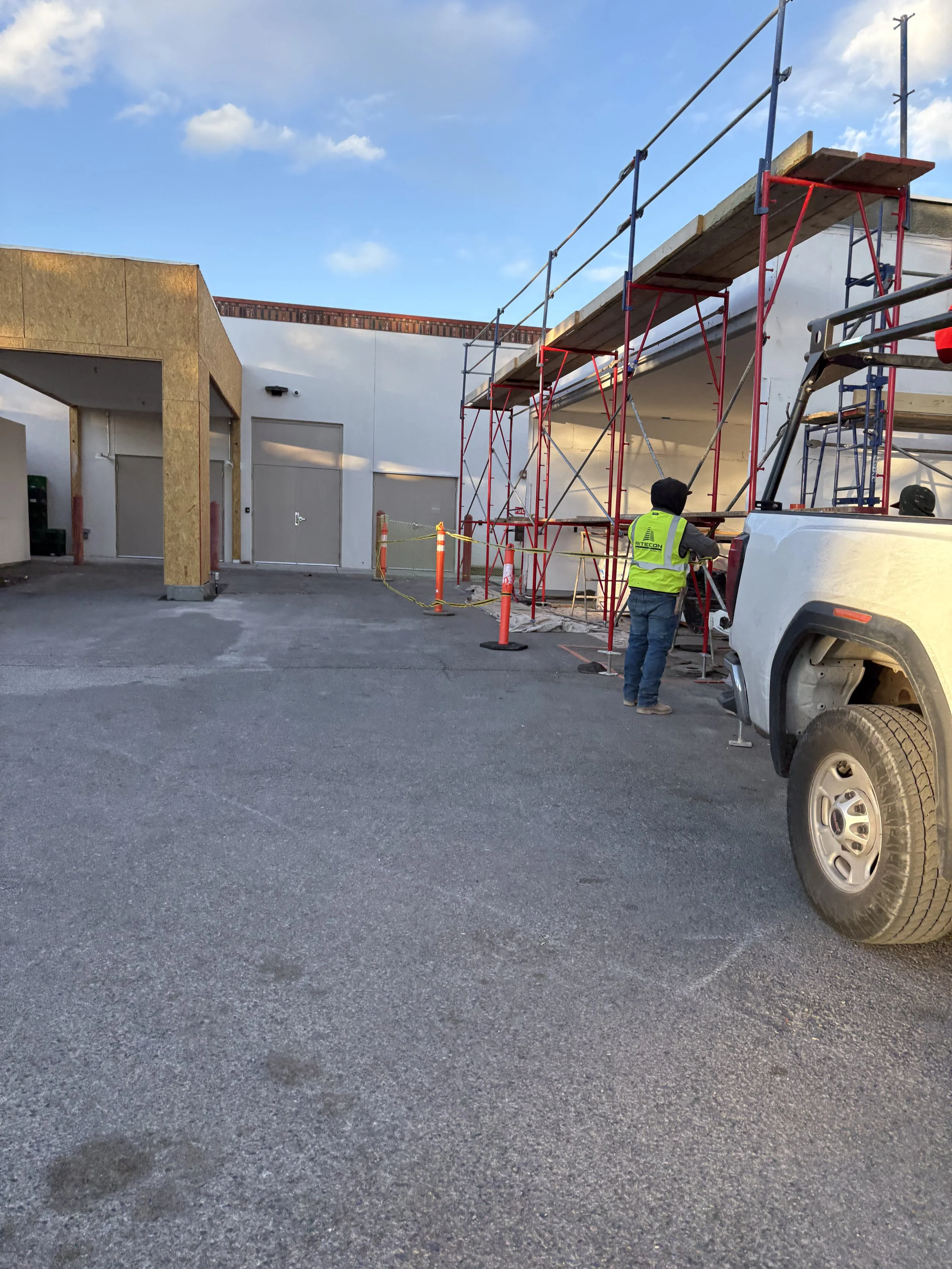 Construction worker in yellow safety vest working on scaffolding outside a building with white walls during daytime.