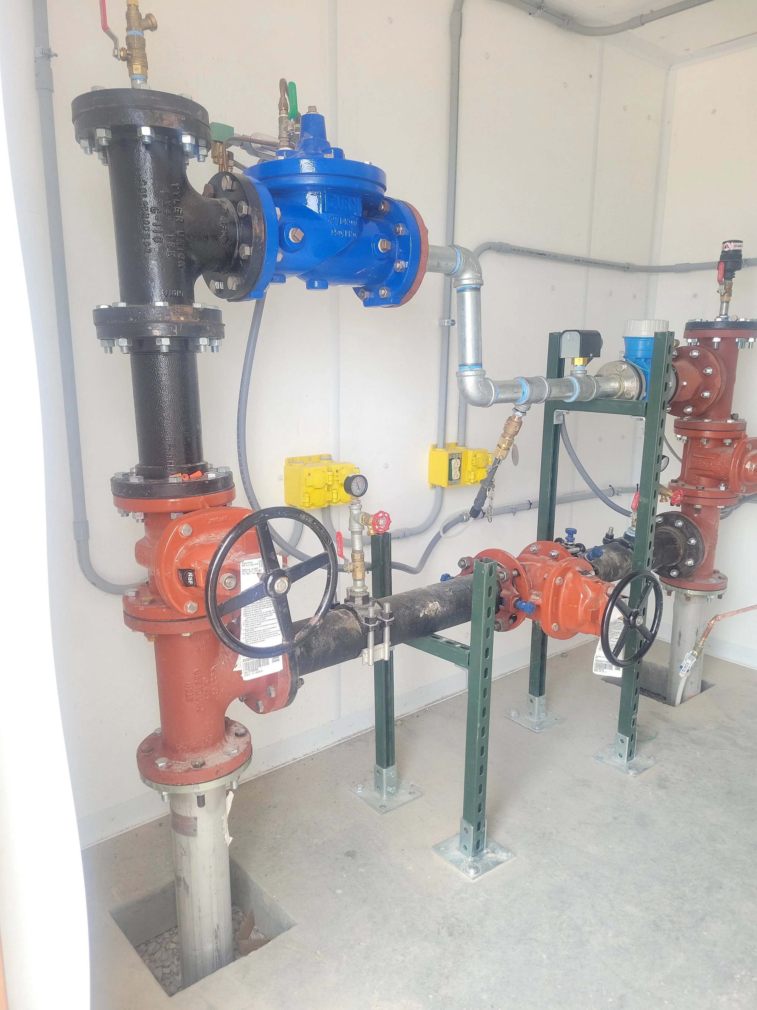 Industrial plumbing system with pipes, valves, and meters mounted on metal supports in a utility room.