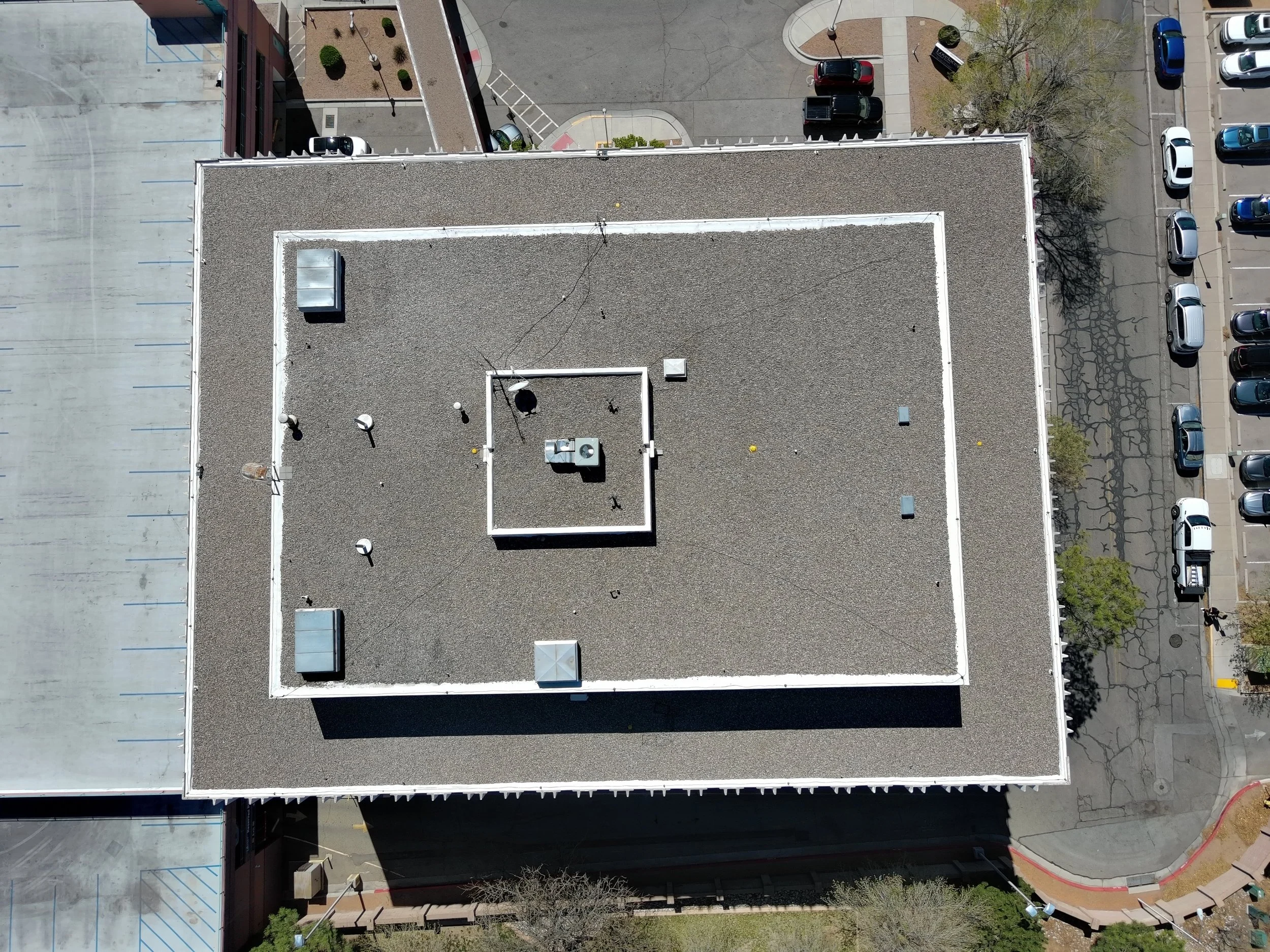 Aerial view of a flat rooftop with HVAC units, vents, antennas, and a small tree outside the building.
