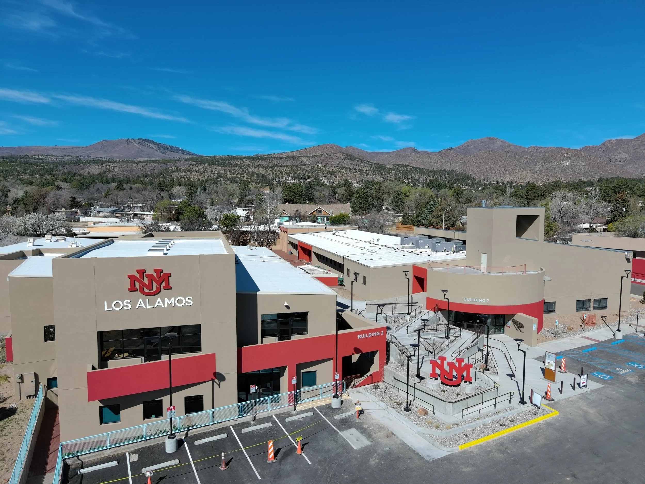 A business building with the University of New Mexico logo, labeled 'Los Alamos,' with mountains and blue sky in the background.