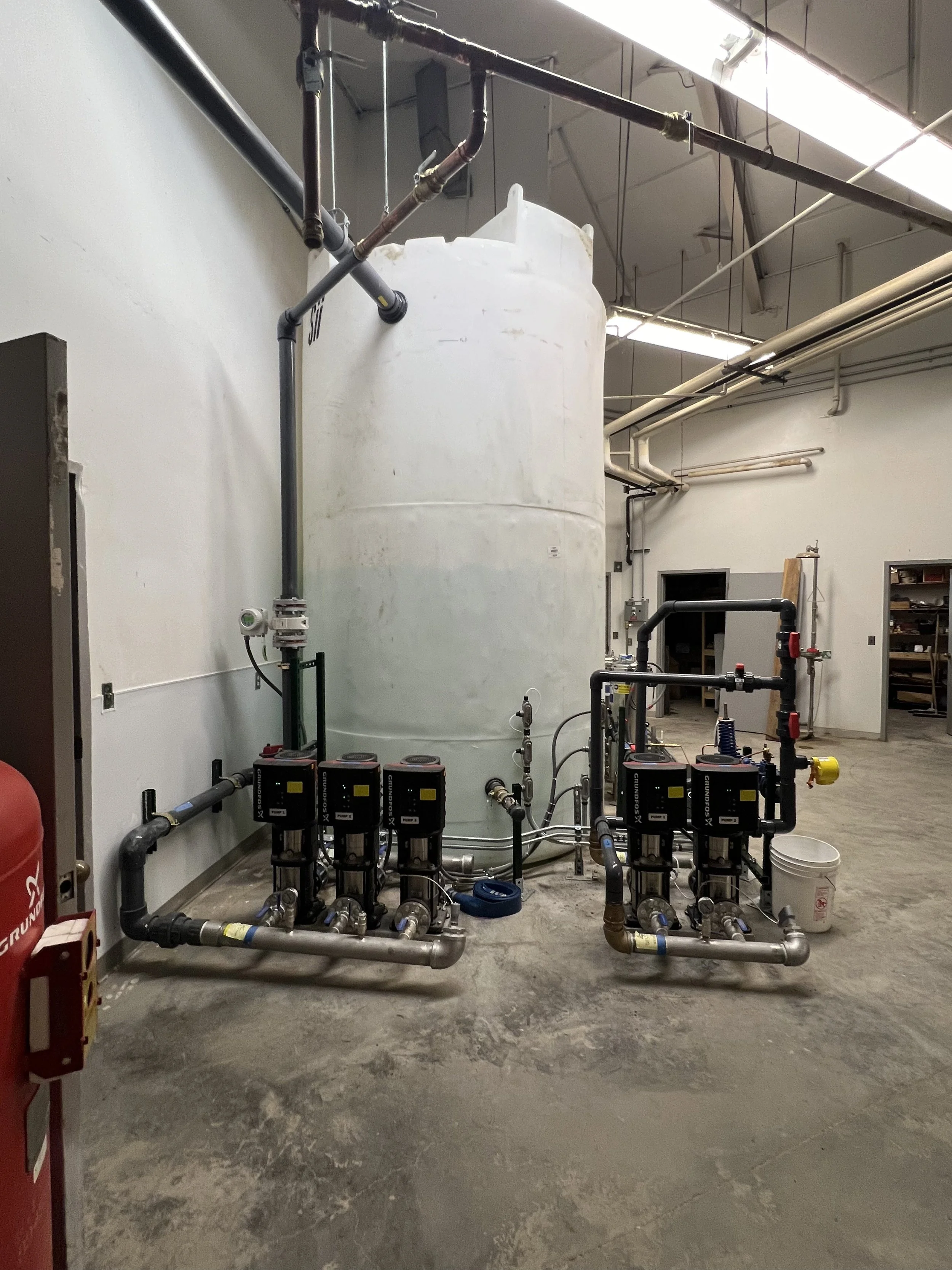 A large industrial water tank connected to various pipes and pumps in a utility room.
