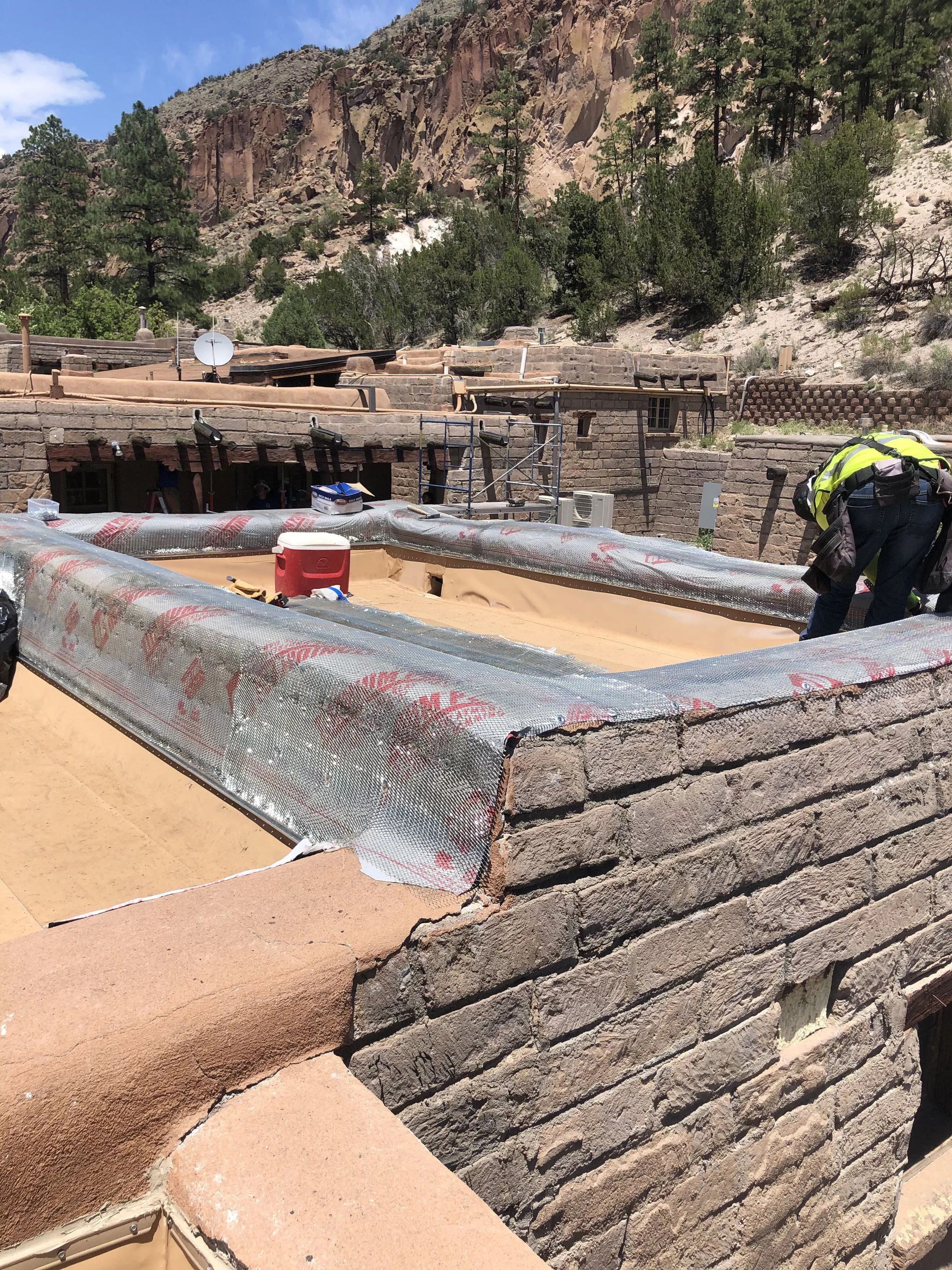 Construction workers assembling a building with brick walls at a rocky, mountainous location, with tools and insulation materials visible.