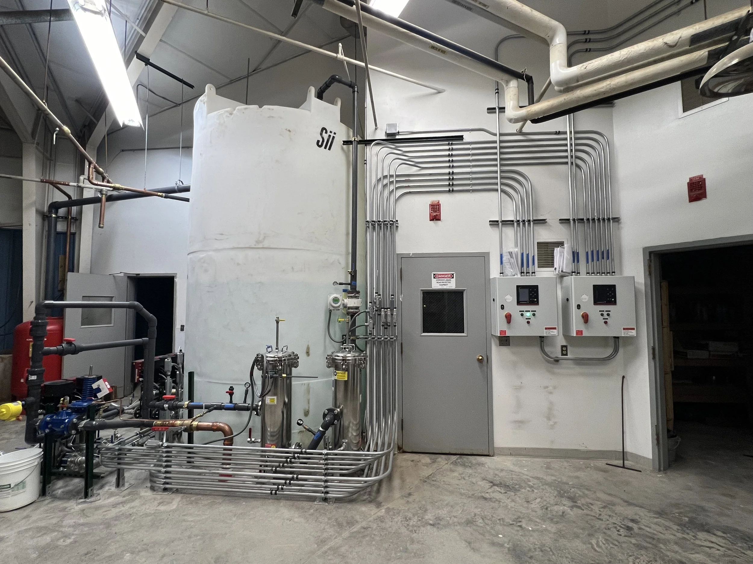 Industrial equipment with pipes, gauges, and control panels in a factory or processing plant.