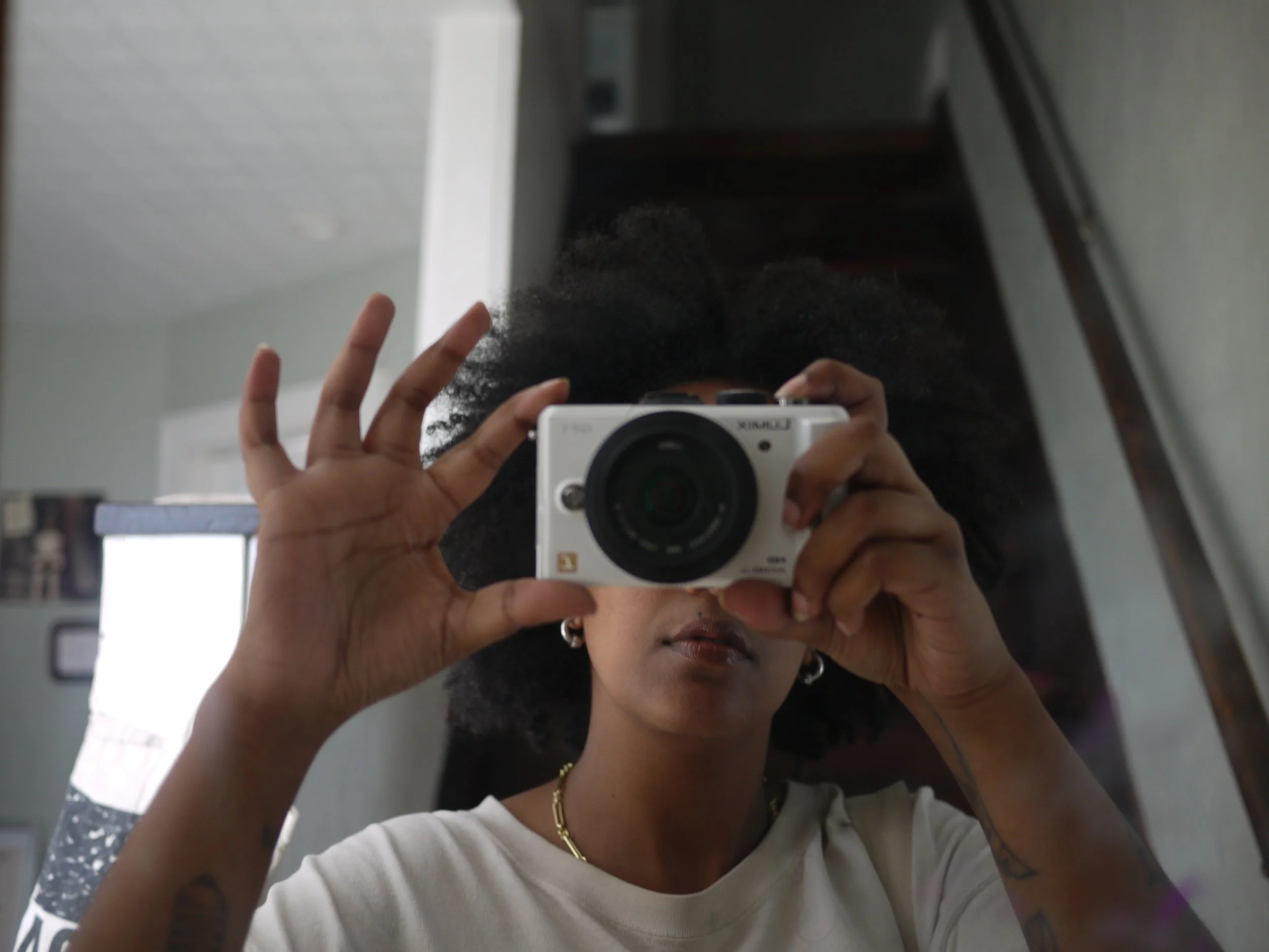 A girl with afro holding a black and white camera taking a mirror selfie